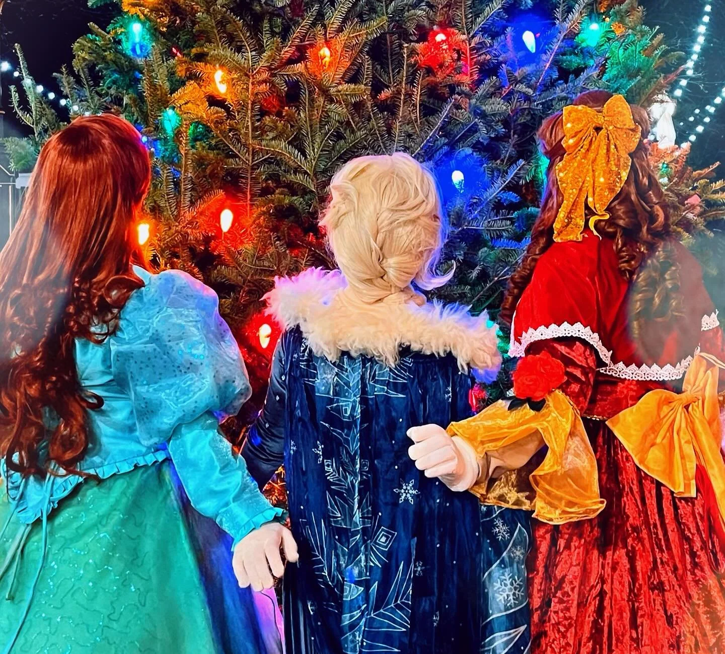Party princesses standing in front of a decorated Christmas tree with colorful lights.