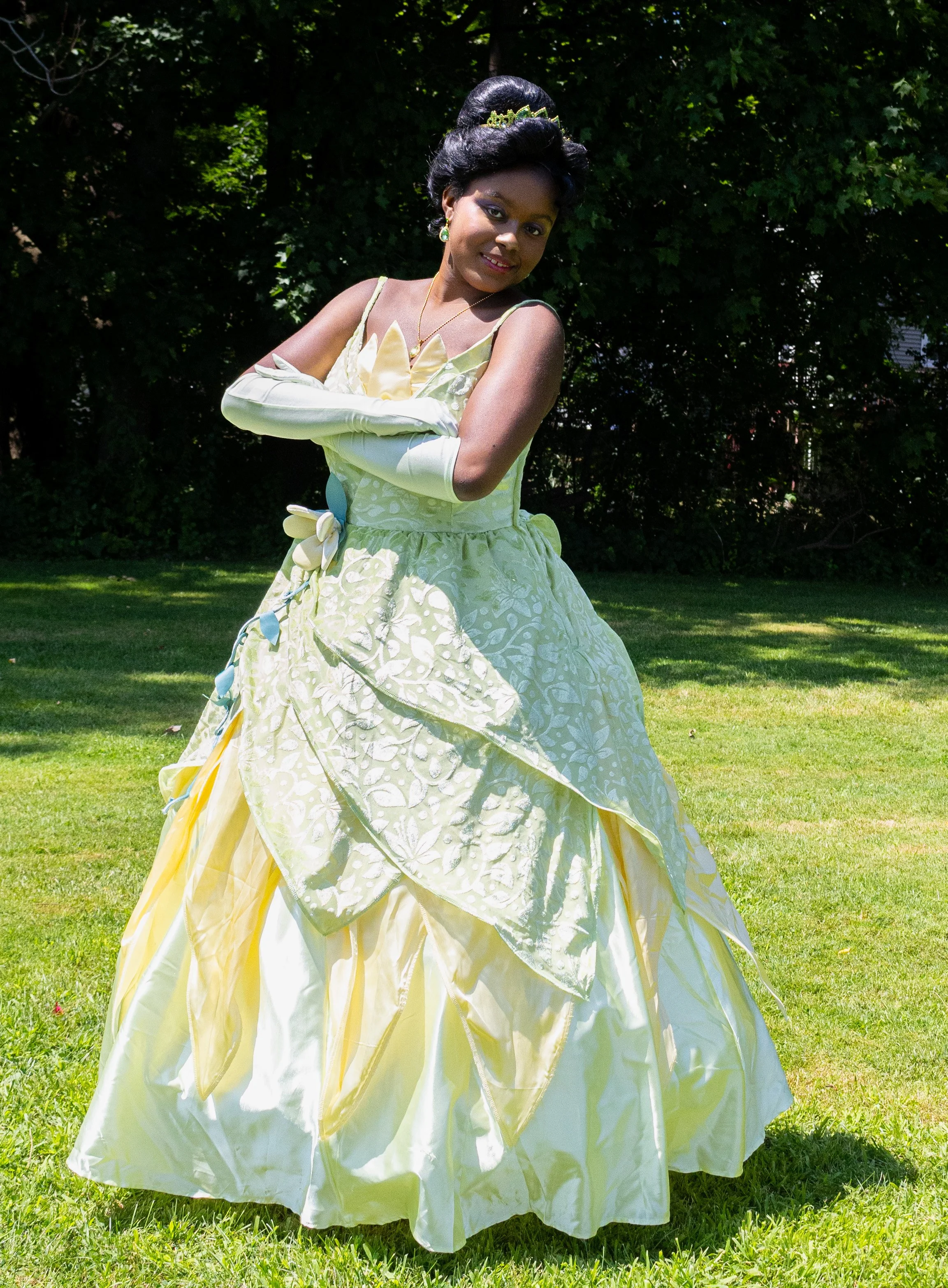 Bayou Princess party character dressed in a yellow and green gown standing outdoors on grass with trees in the background.