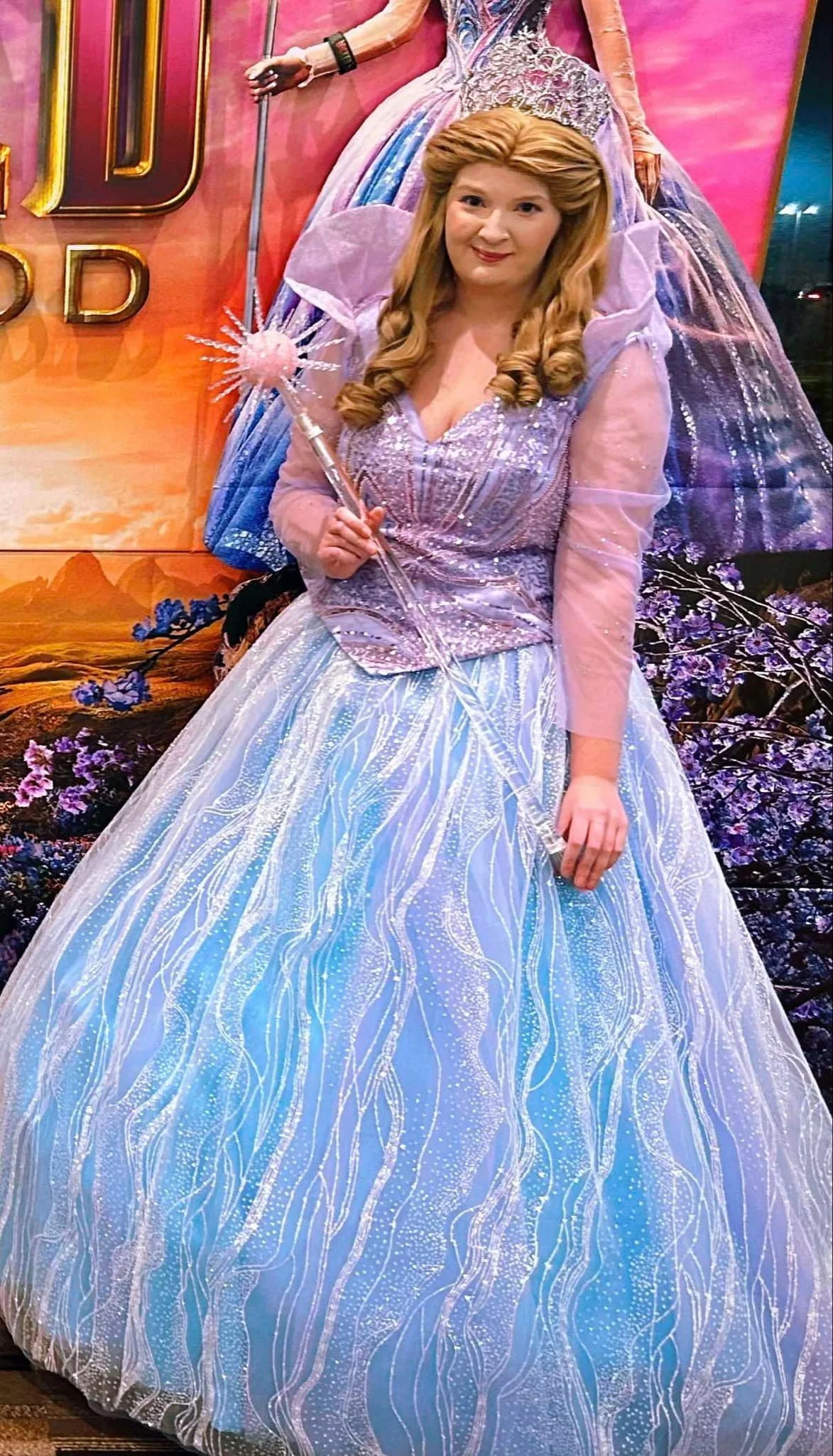 Bubble Witch party princess wearing a sparkly blue and silver gown, with long curly blond hair, holding a magic wand, standing in front of a colorful fantasy backdrop.