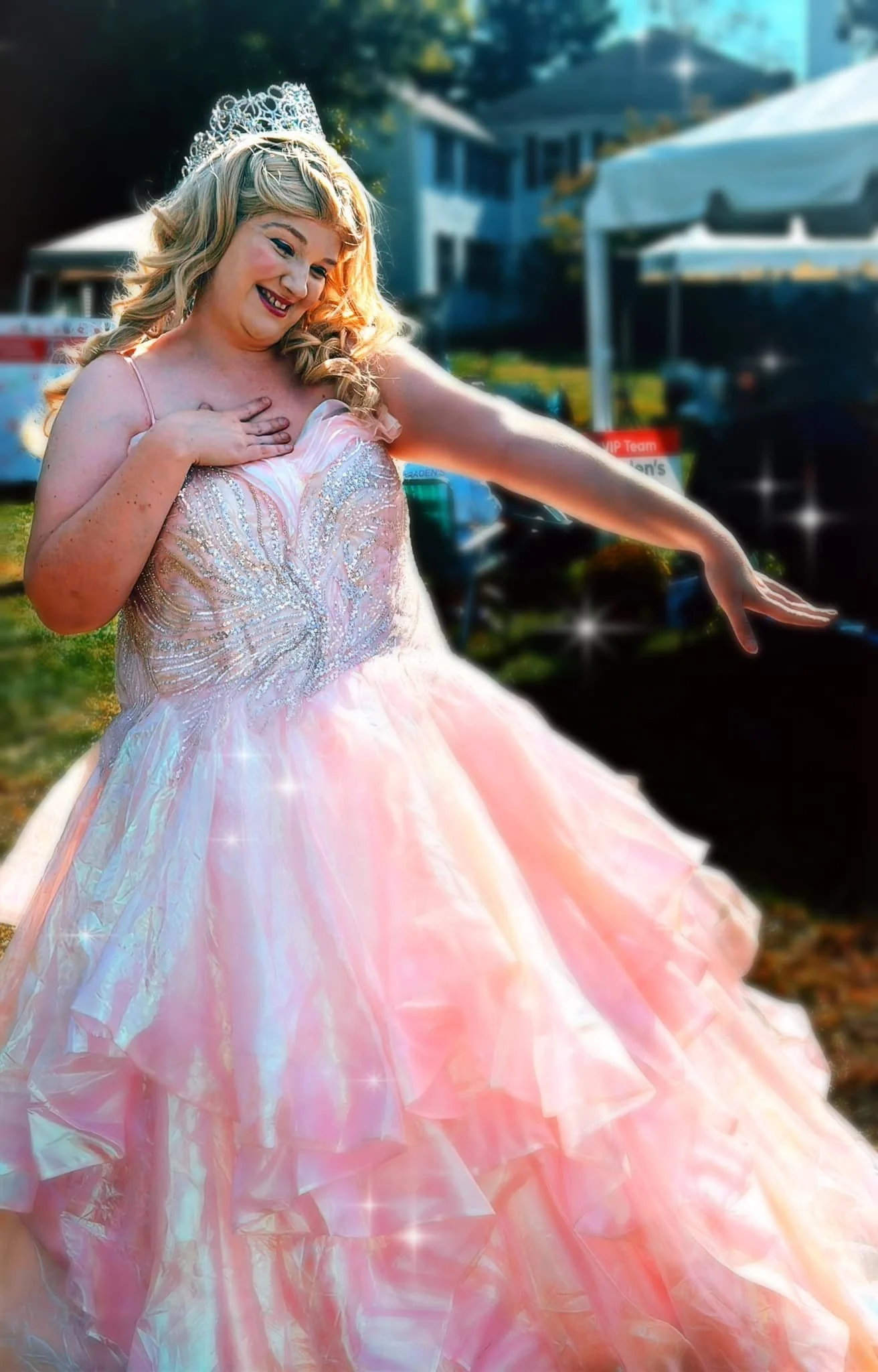Bubble Witch party princess in a pink gown with a tiara, smiling and posing outdoors with one hand on her chest and the other extended.