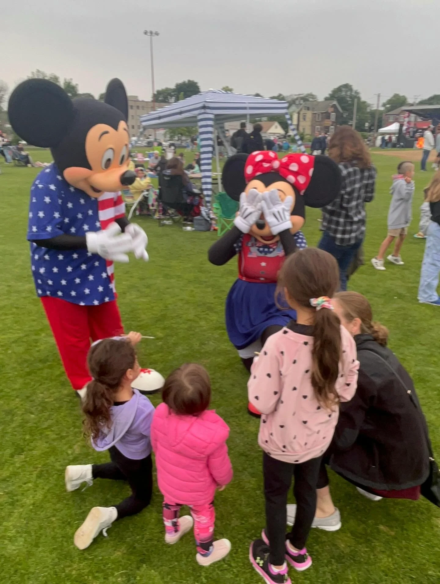 Mr. and Miss Mouse party characters entertaining children at an outdoor event, with kids sitting on the grass watching.