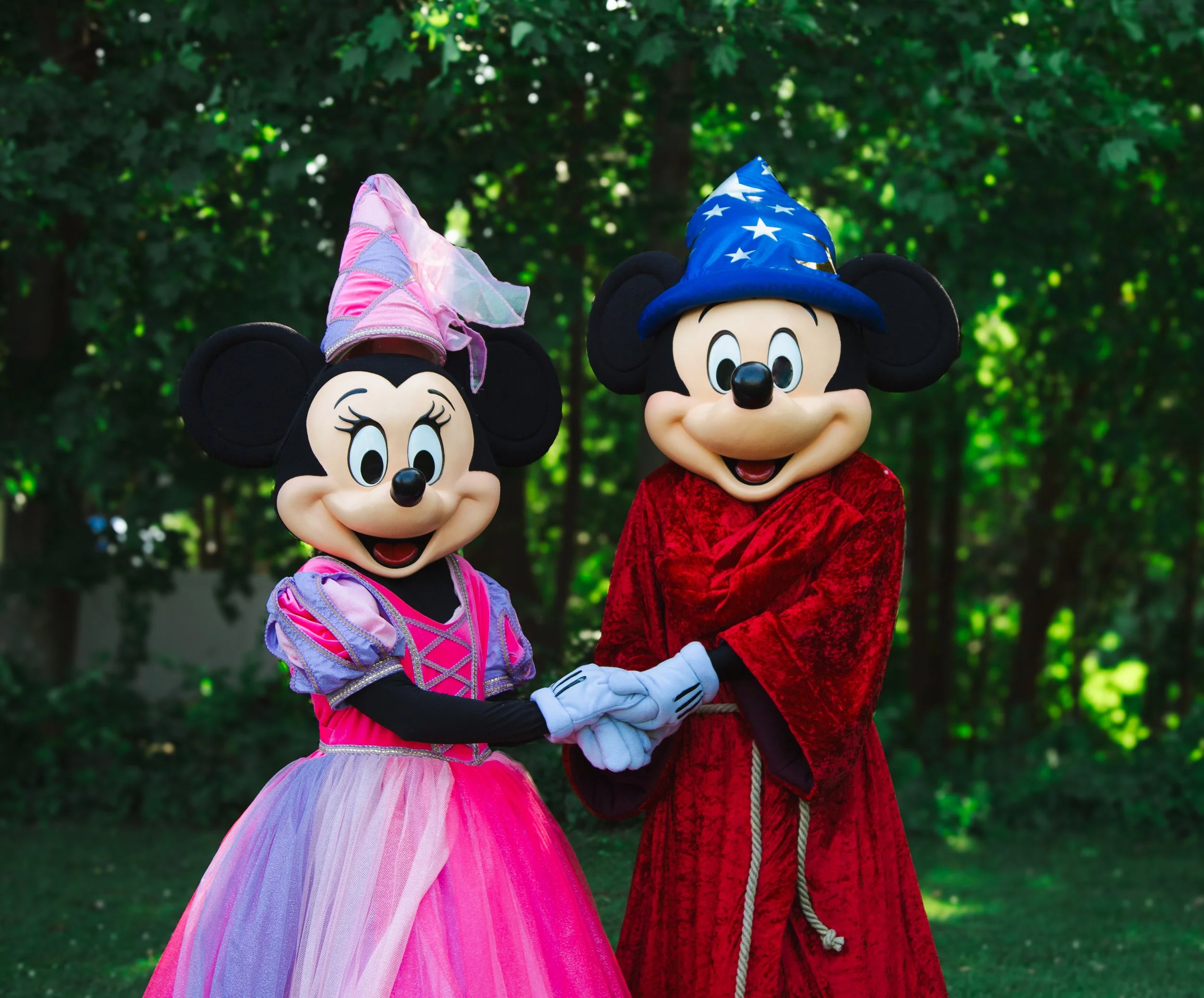Mr and Miss Mouse party characters, holding hands outdoors with green trees in the background.