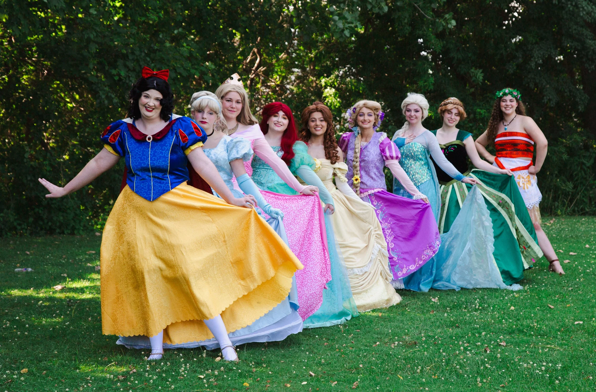 Party Princesses standing outdoors on grass with trees in the background.