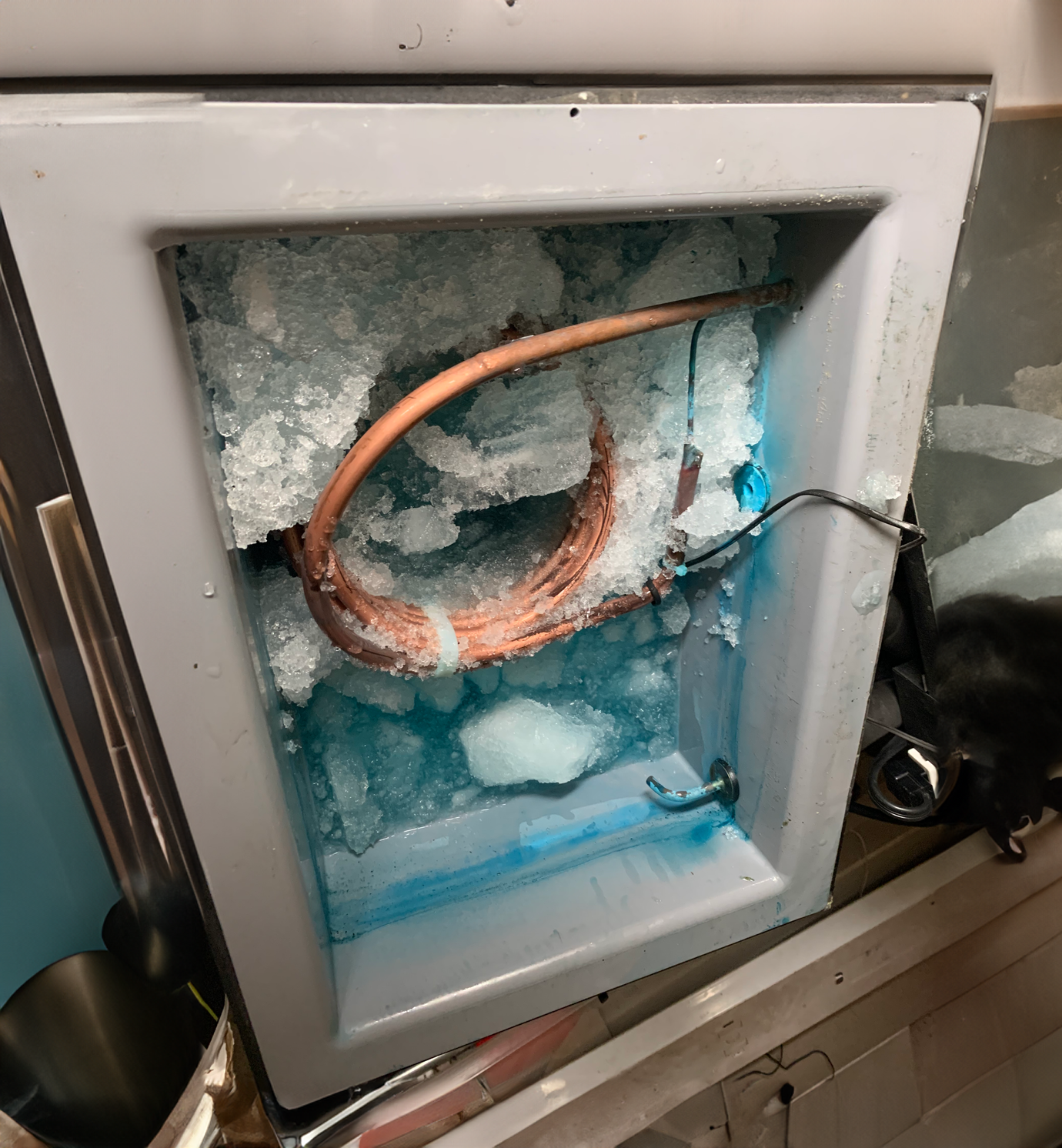 A washing machine door open with ice and frozen copper pipes inside, indicating an ice build-up or damage.