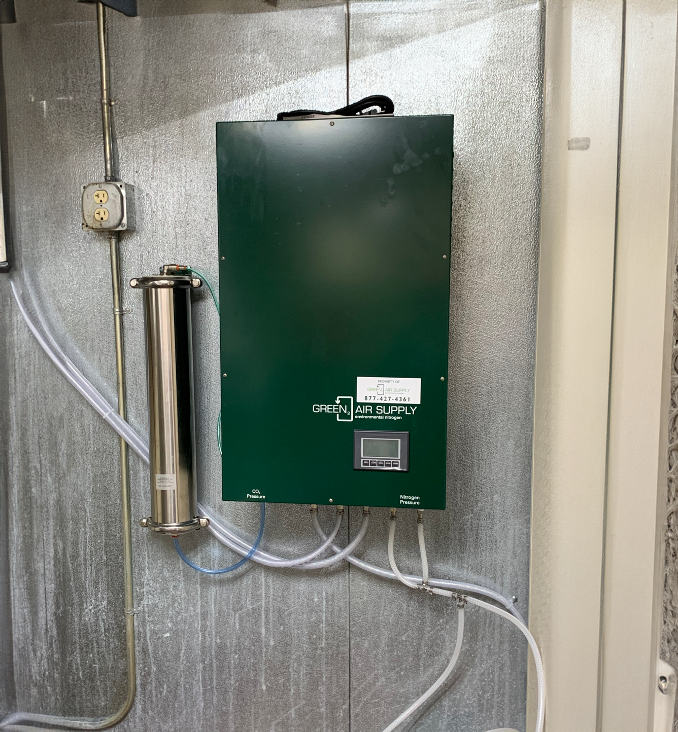 Green environmental nitrogen system with digital display, pipes, and wires on a wall.