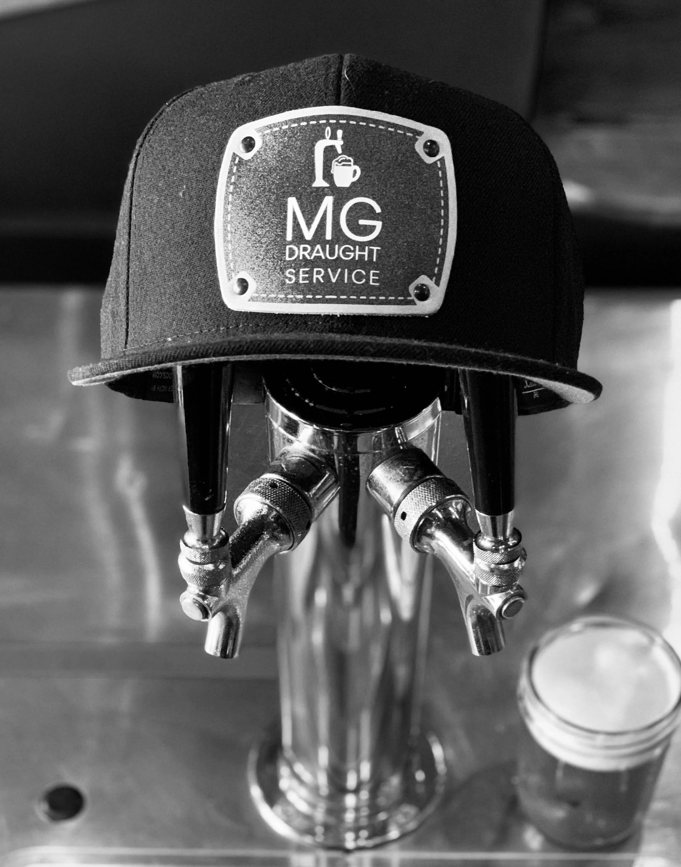 A close-up view of a metal fixture with a sign that says 'MG Draught Service' and shows a tap pouring beer into a mug, mounted on a cylindrical surface.