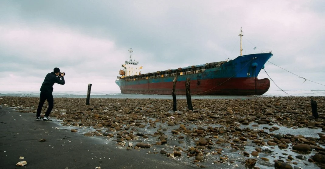 A man photographing a cargo ship. Image Credit: Photo by Andrew Leu on Unsplash