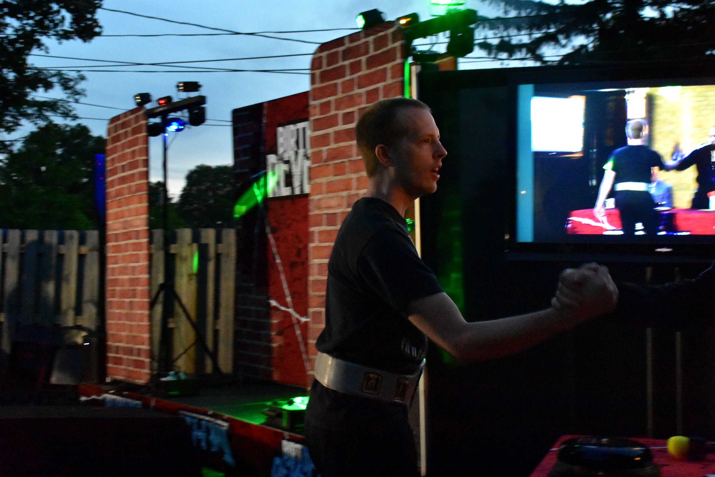 Person shaking hands in front of a video screen outdoors with stage lighting.