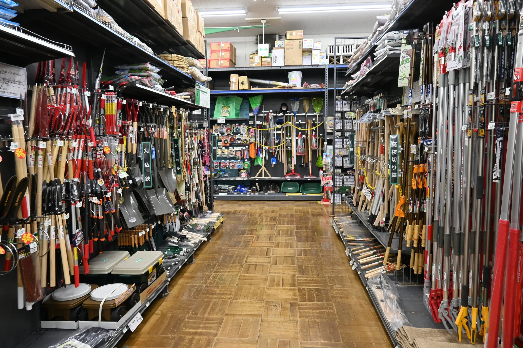 A hardware store aisle displaying gardening tools such as shovels, rakes, and hoes, with shelves stocked with various gardening supplies and accessories.