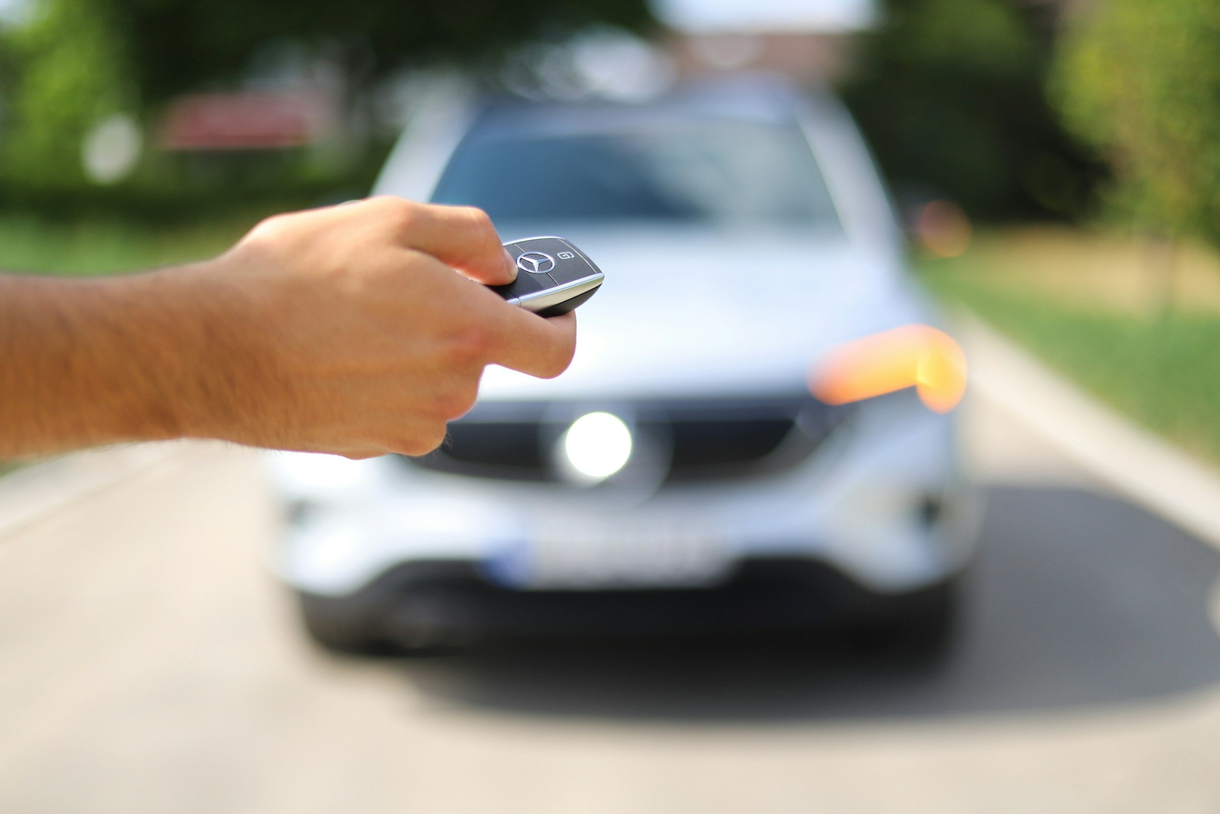 Person holding a Mercedes-Benz car key in front of a silver Mercedes-Benz SUV on a suburban street.