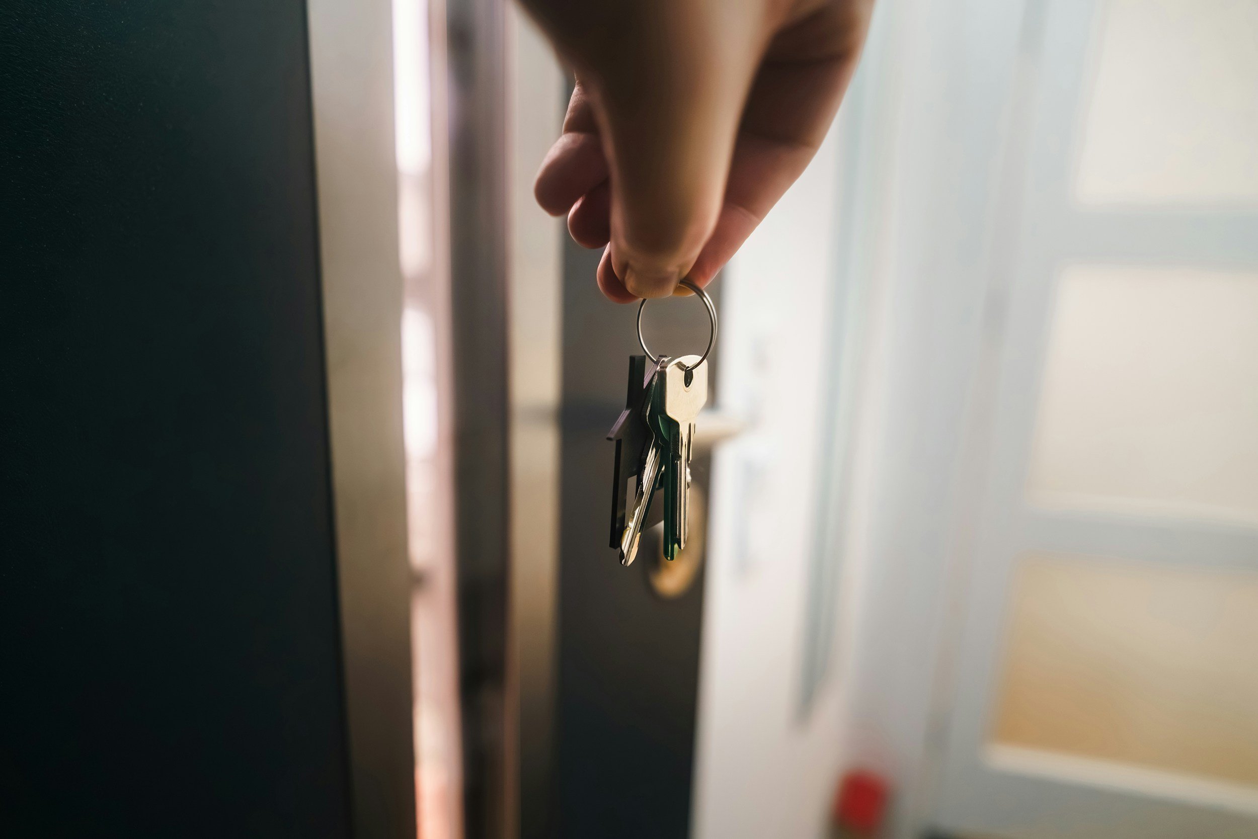 A hand holding a set of keys with various keychains, positioned near a dark-colored mailbox or lockbox.