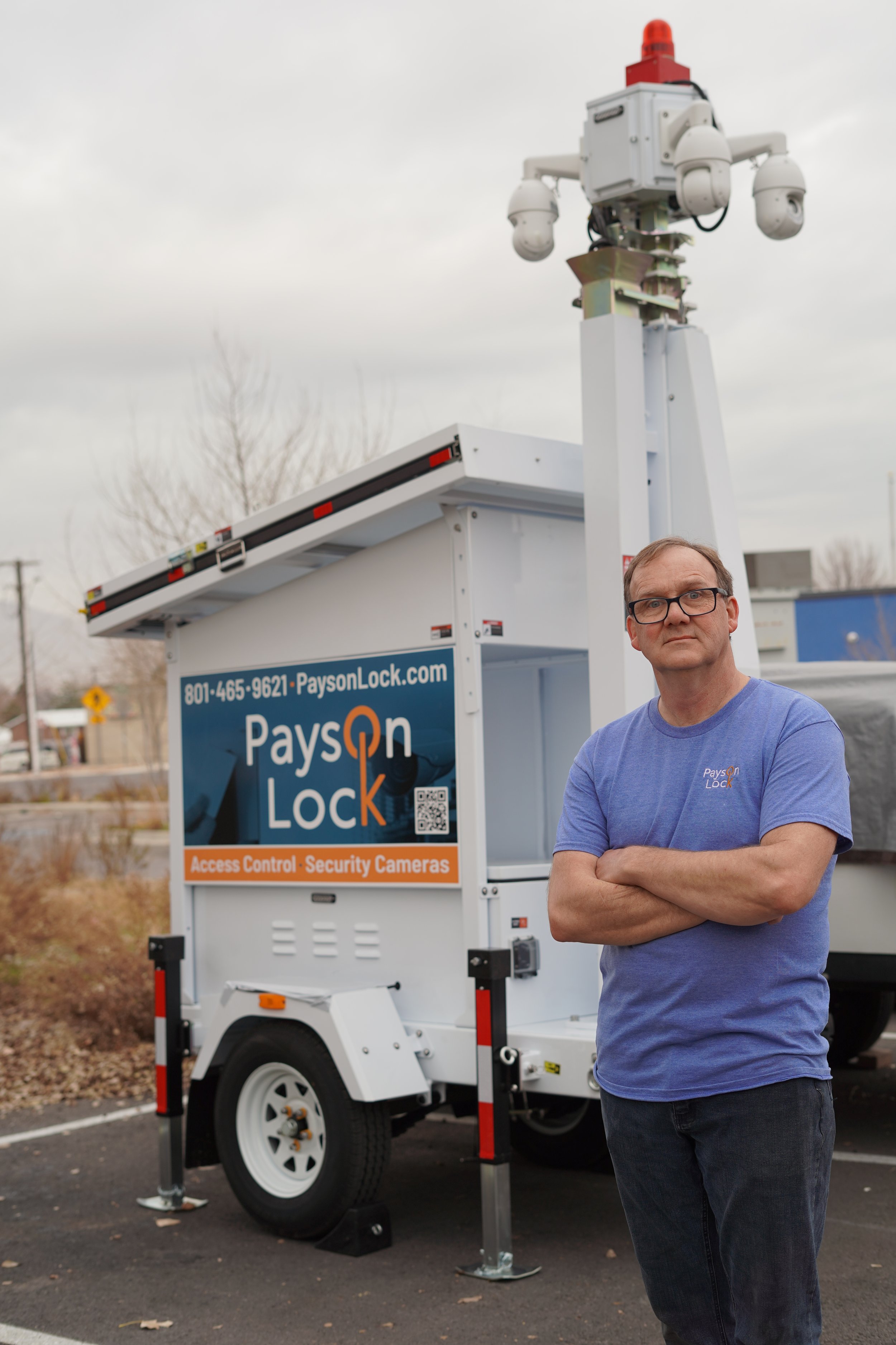 A locksmith standing by a portable camera cctv system on a trailer.