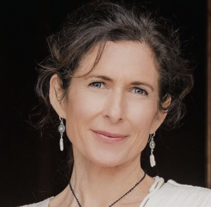 A woman with short, wavy gray hair, blue eyes, and earrings, smiling at the camera.