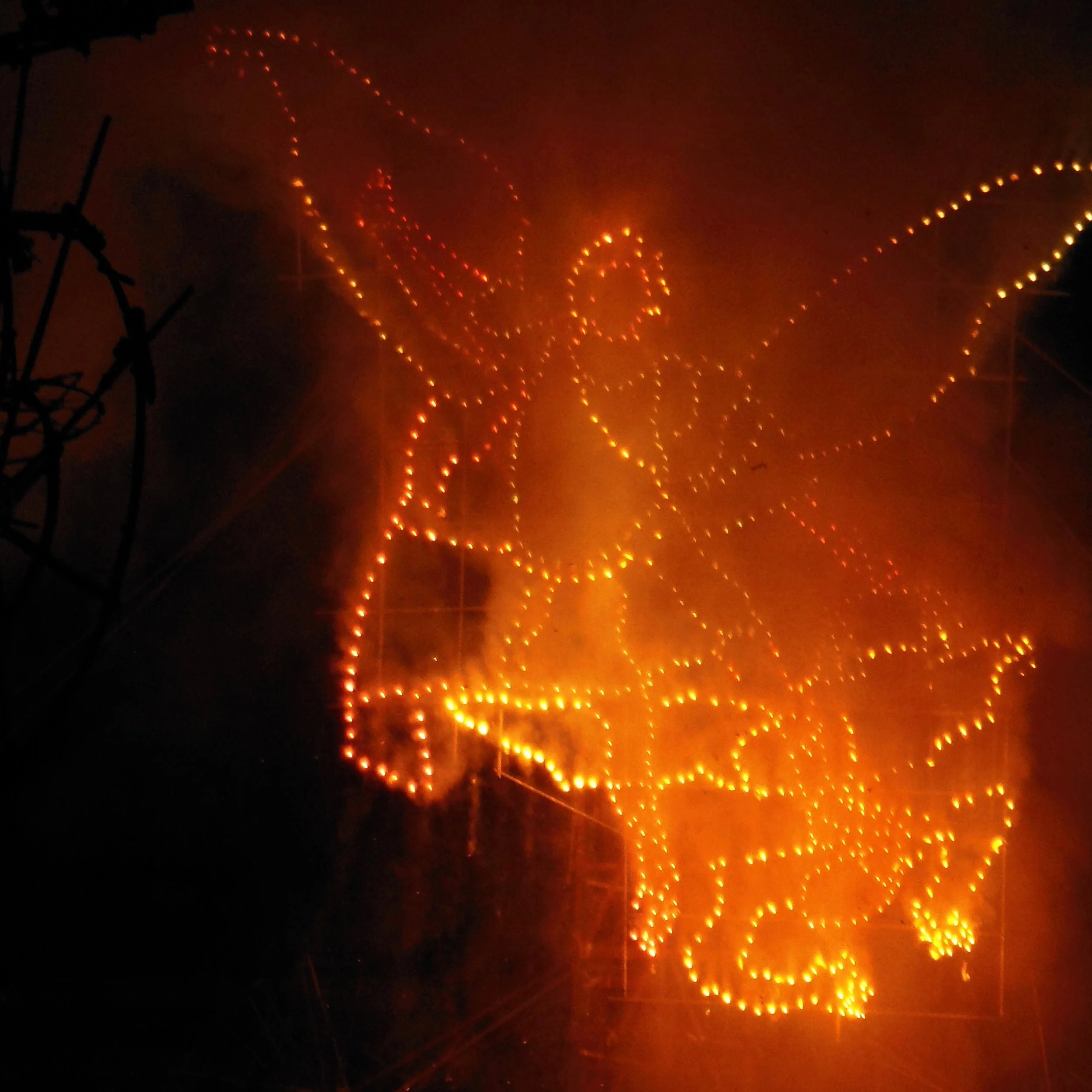 Bright orange and yellow lights arranged in intricate patterns on a dark sky, possibly from a night-time light display or fireworks.