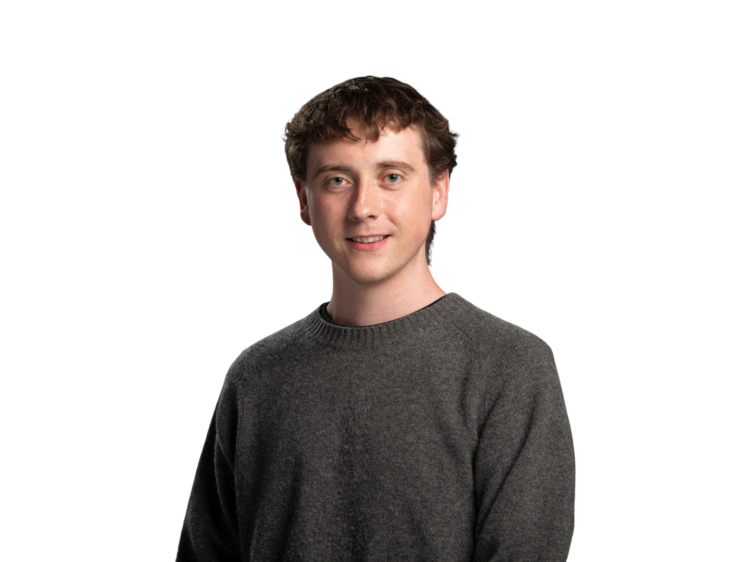 Young man smiling, wearing a beige button-up shirt, standing against a black background.