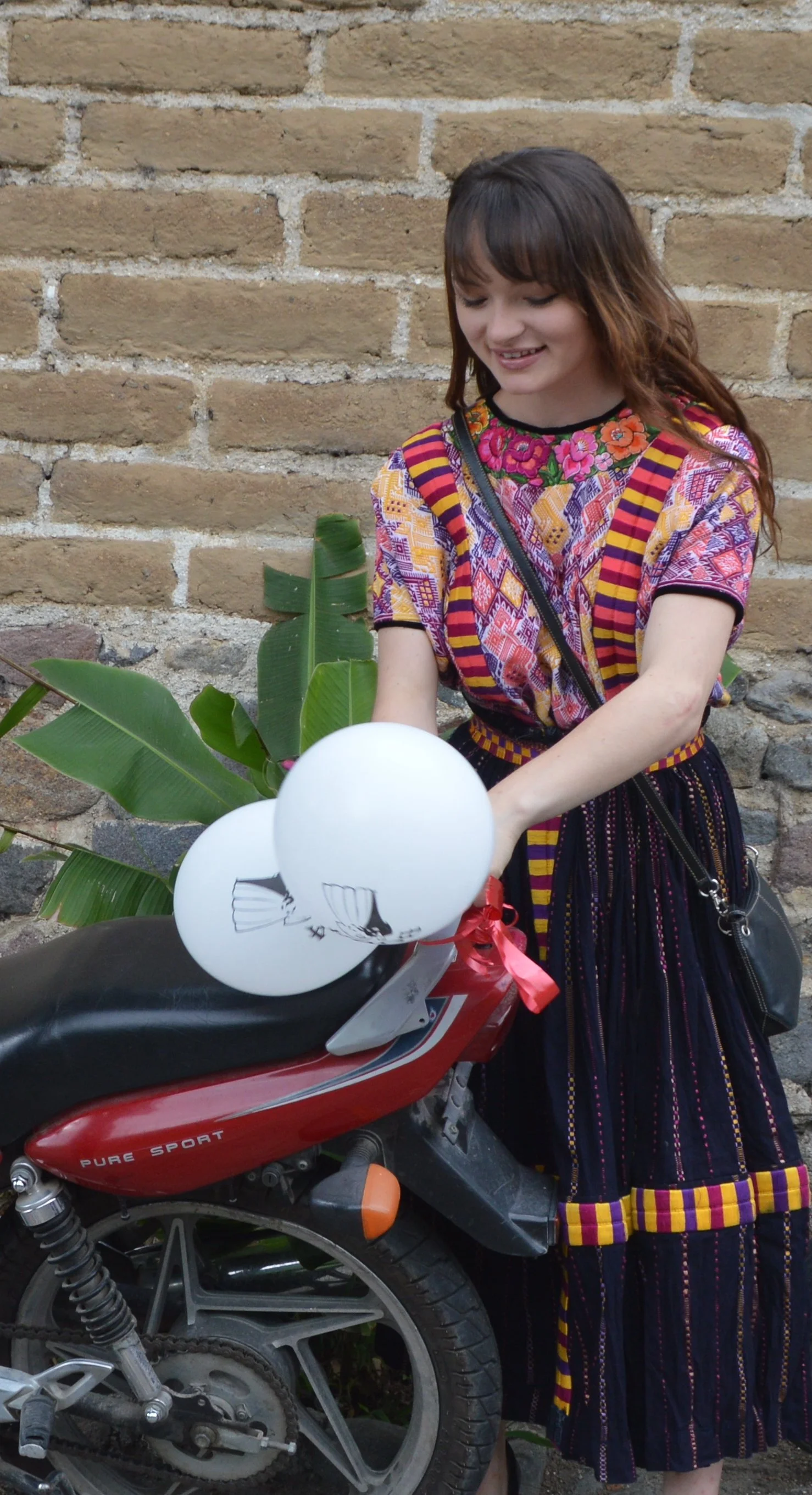 A woman in traditional clothing standing next to a motorcycle decorated with white balloons and green leaves.