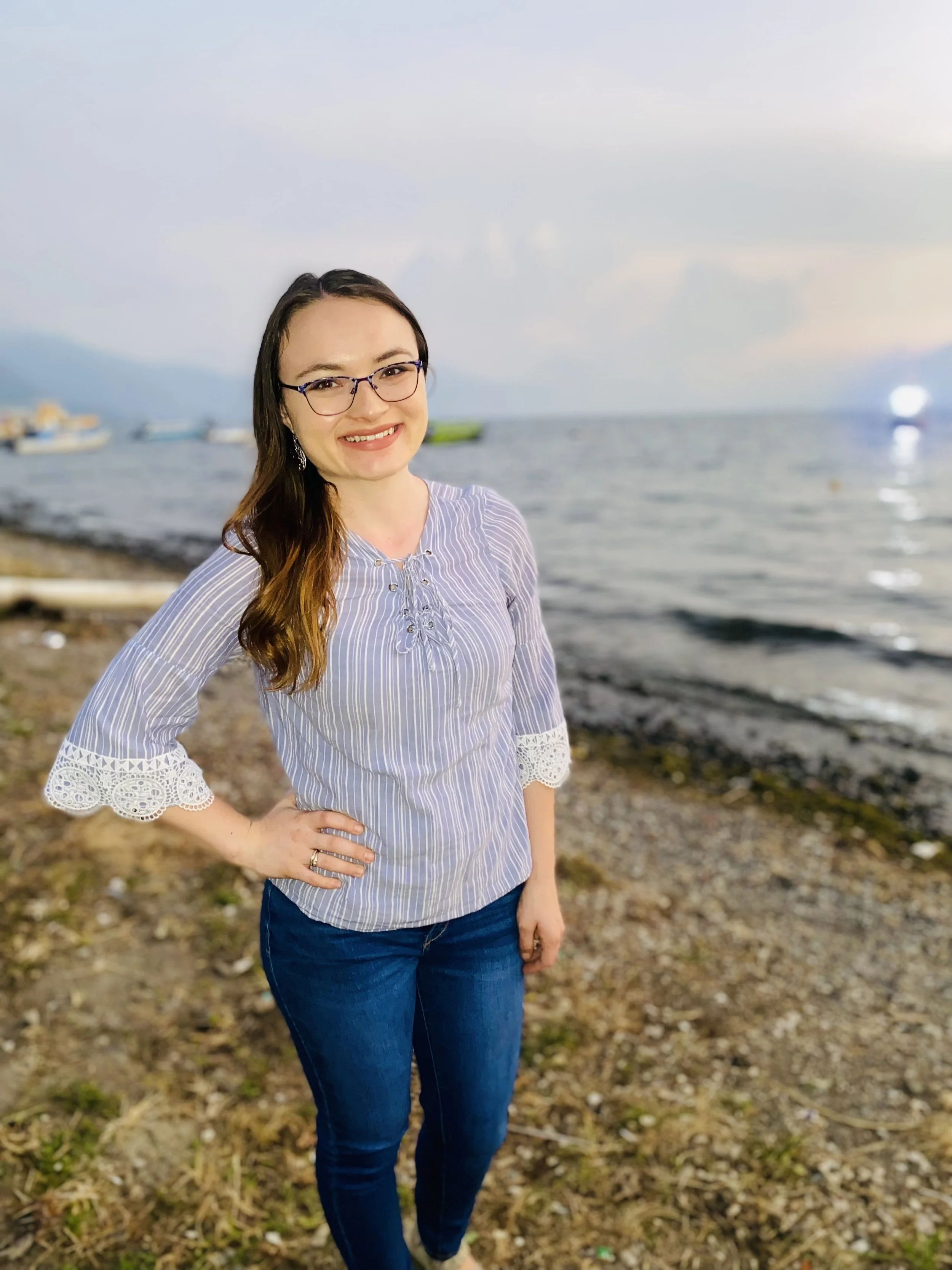 Woman smiling near a lake with a mountainous background.