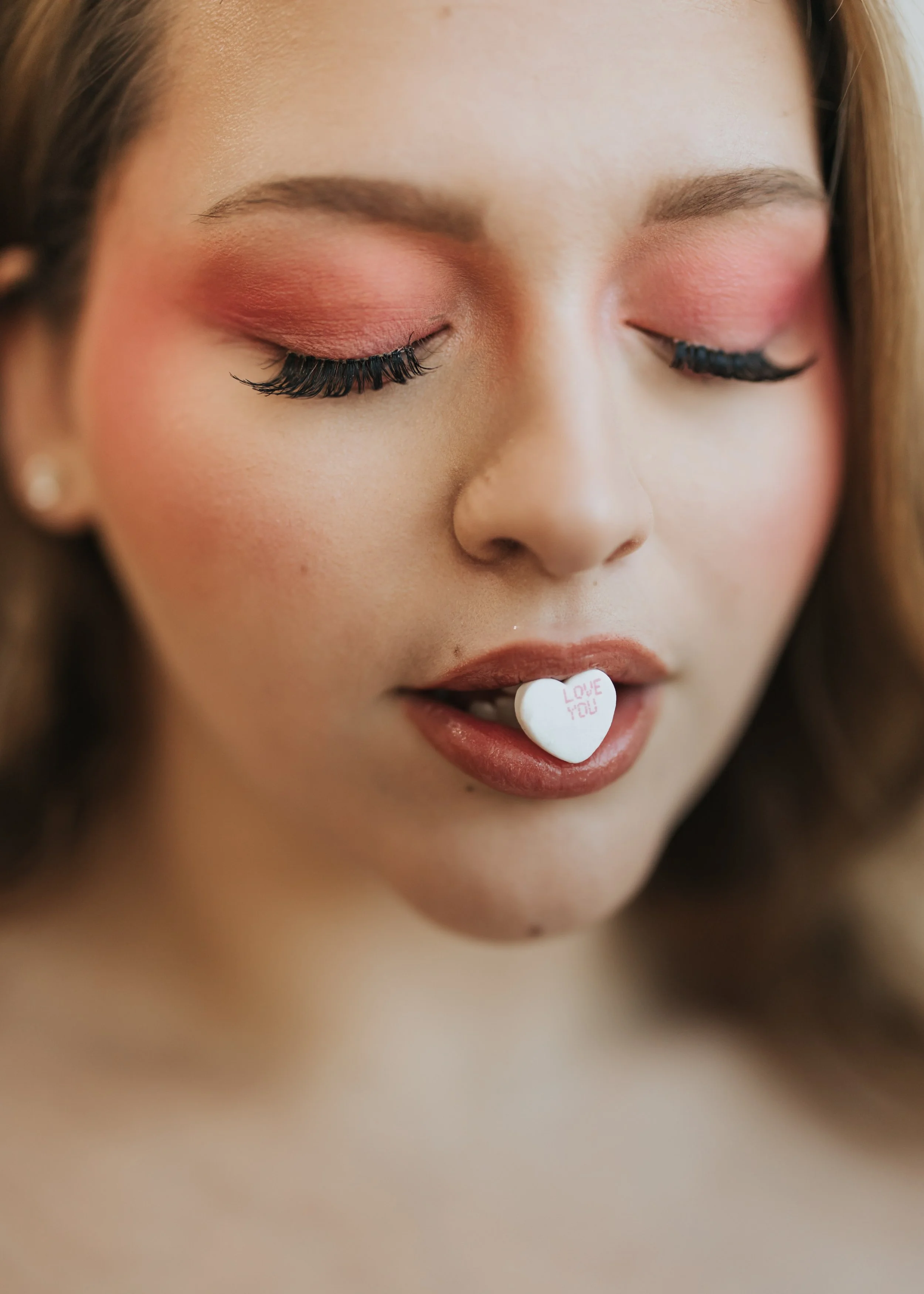  Close up photo of model with candy heart in her mouth for a creative Valentine’s Day fashion photoshoot. 