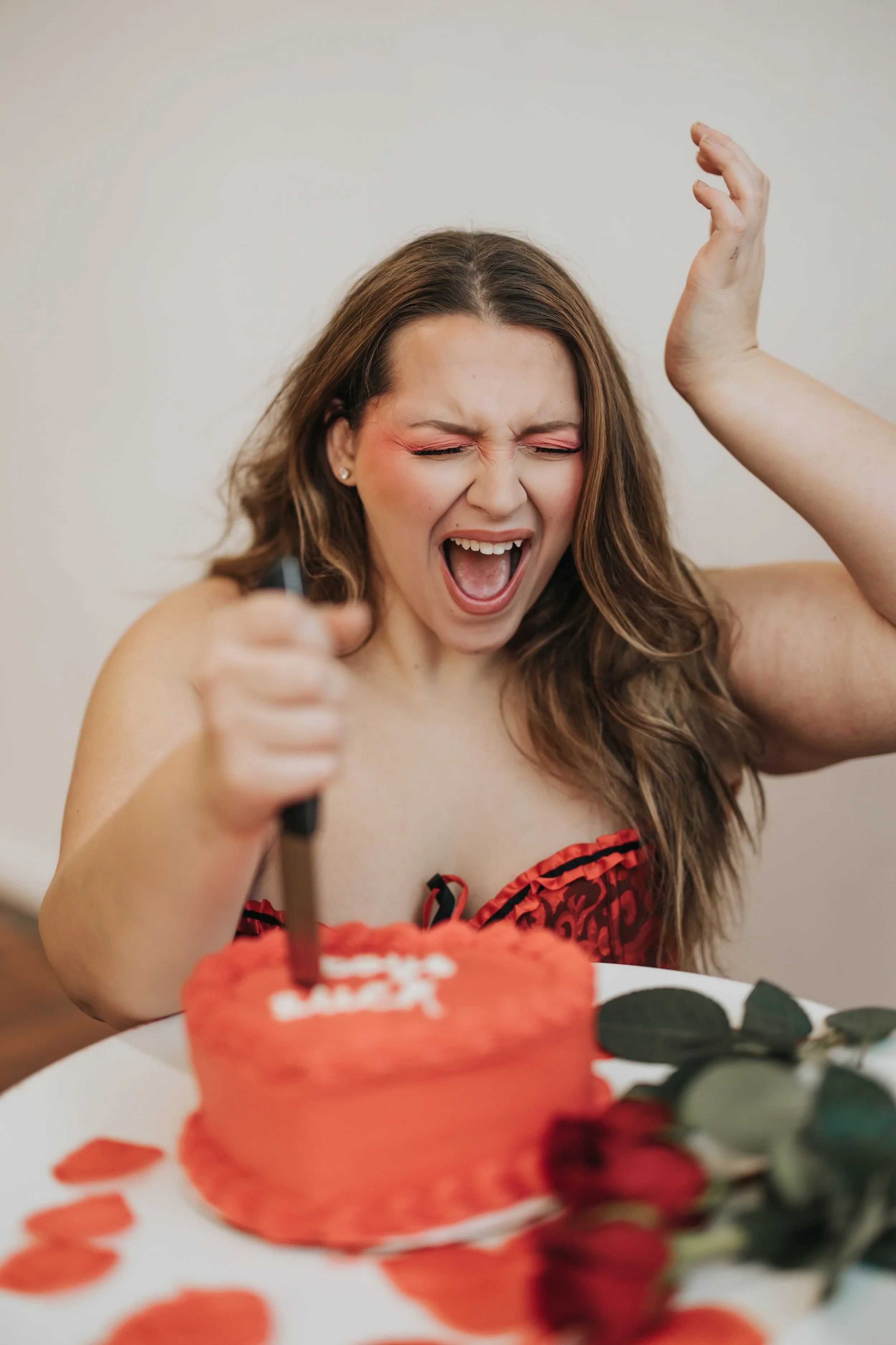  Fashion model poses with an emotional expression while stabbing a knife in a heart-shaped cake for a creative Valentine’s Day photoshoot. 