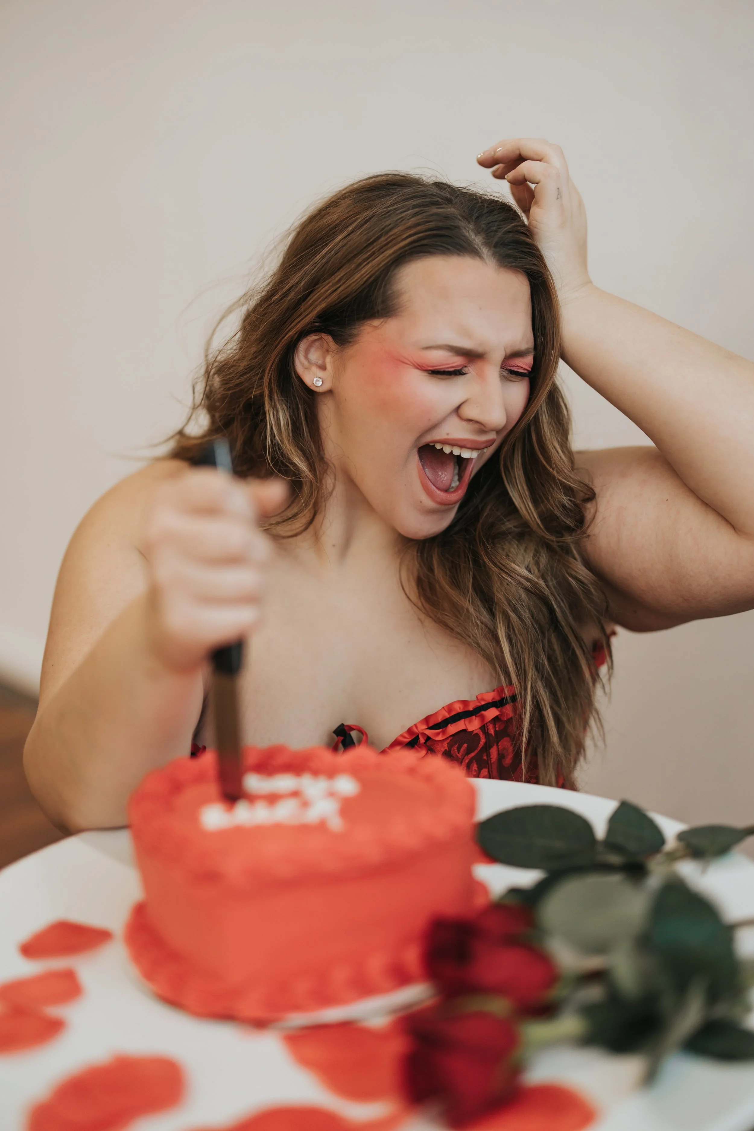  Fashion model poses with an emotional expression while stabbing a knife in a heart-shaped cake for a creative Valentine’s Day photoshoot. 