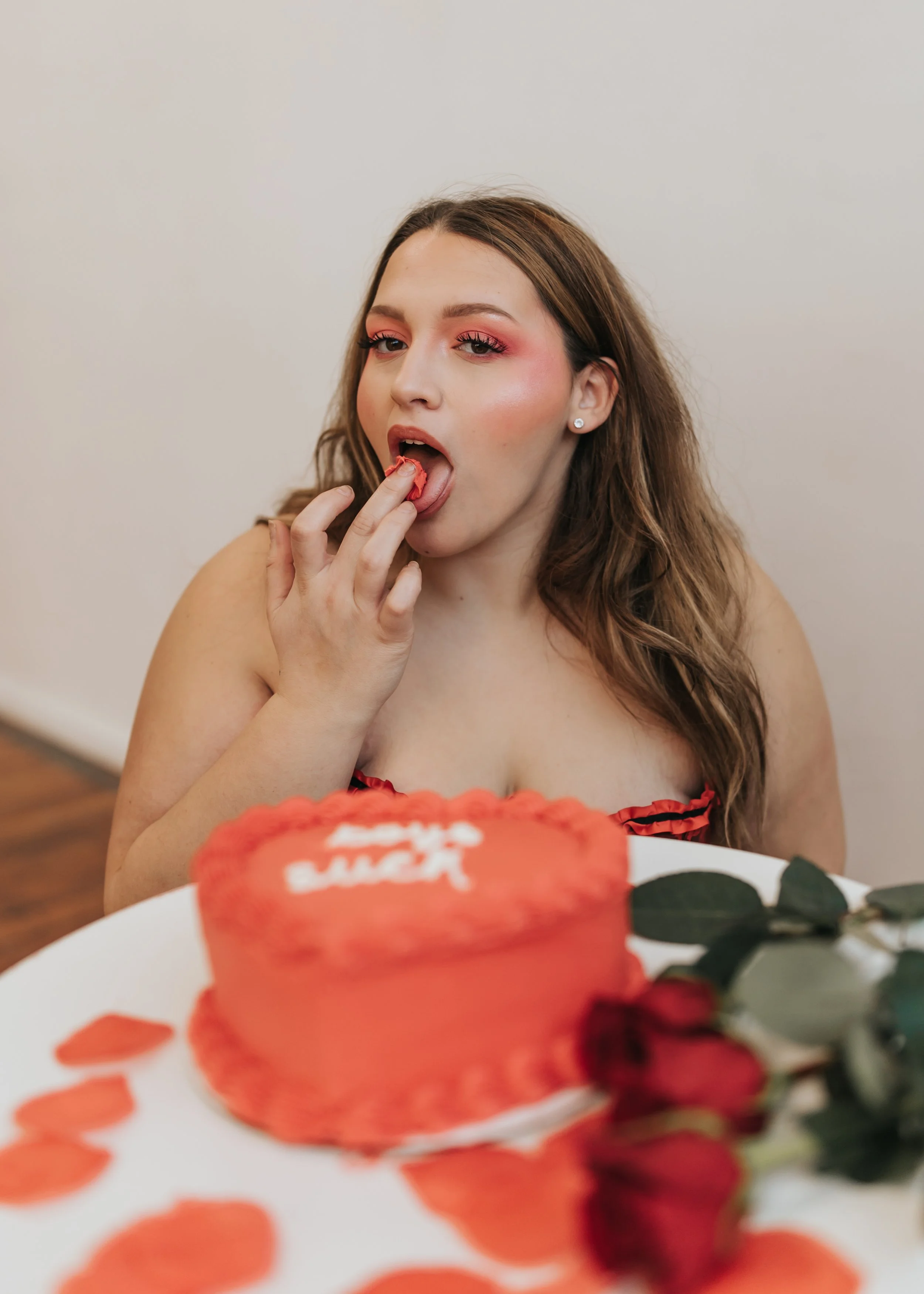  Fashion model poses with a heart-shaped cake while licking frosting from her hands for a creative Valentine’s Day photoshoot. 
