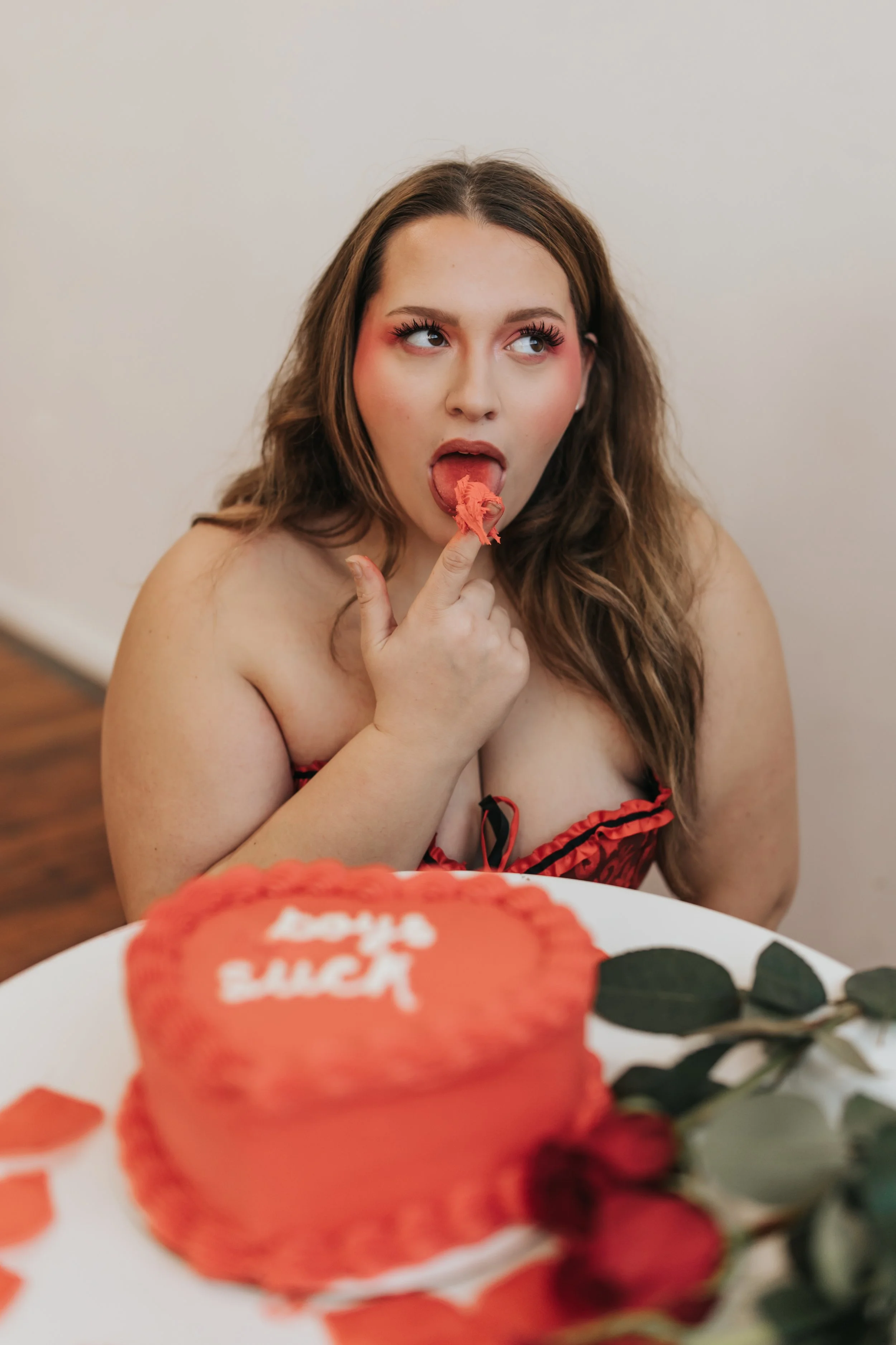  Fashion model poses with a heart-shaped cake while licking frosting from her hands for a creative Valentine’s Day photoshoot. 