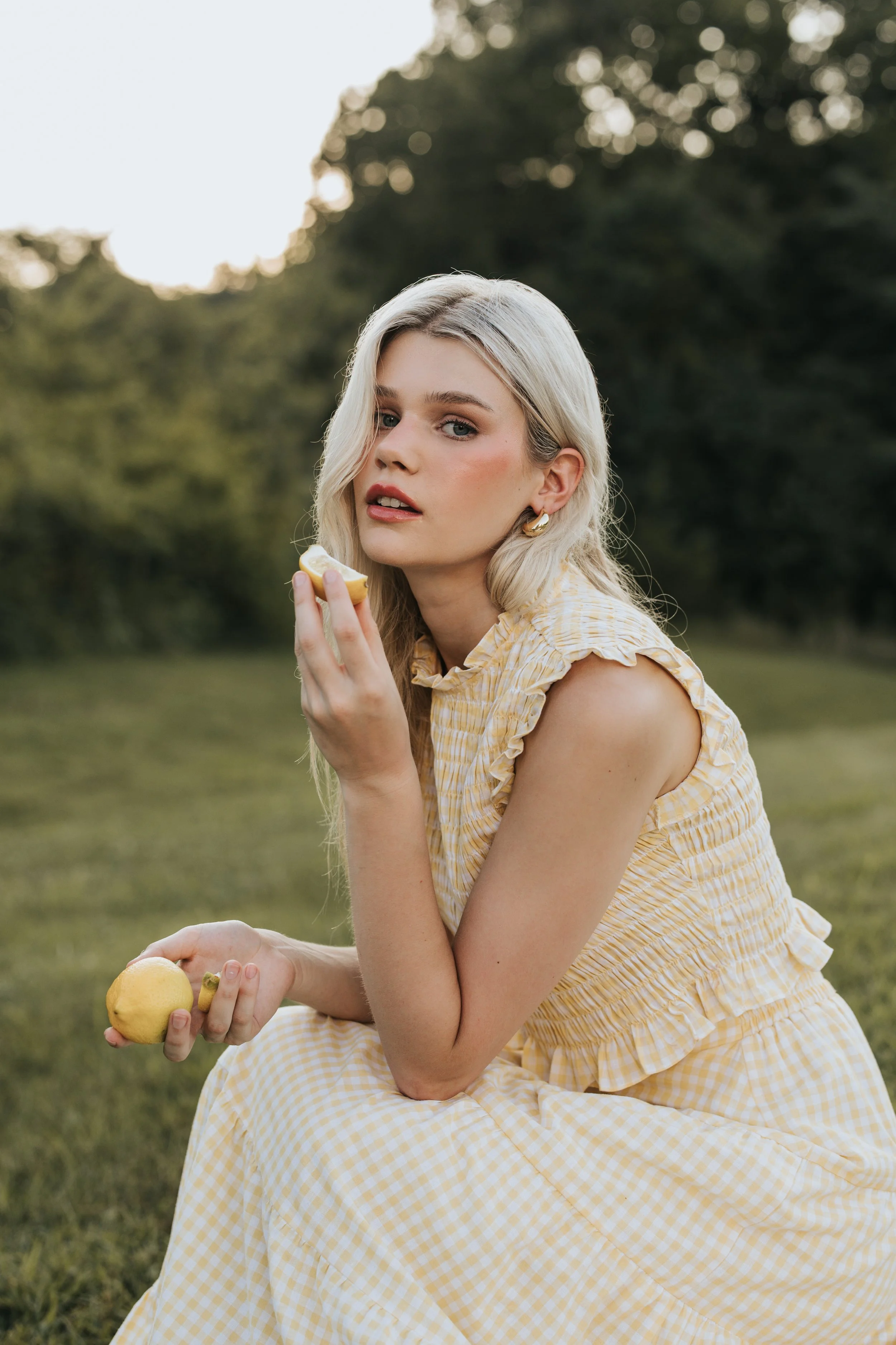  Blonde model poses in the grass holding a lemon during her fashion photoshoot. 