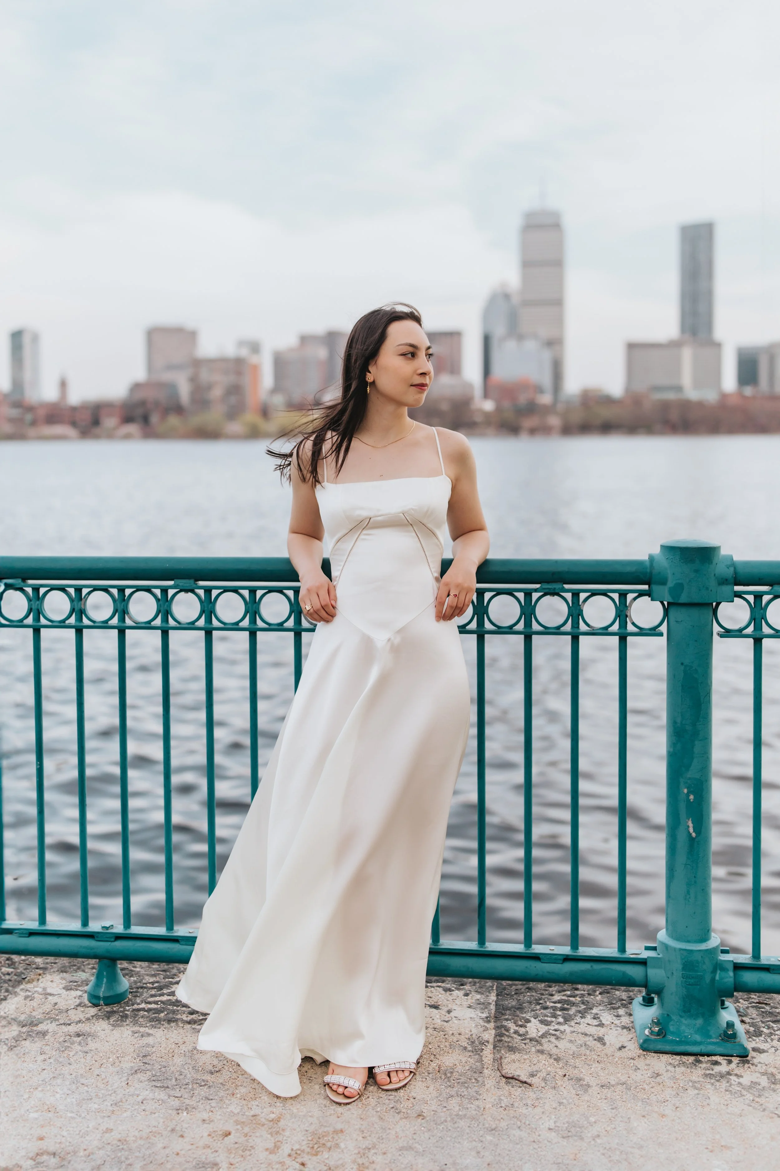  Claire, an MIT graduate, poses for her Boston graduation photos in a long white dress against the Boston skyline 