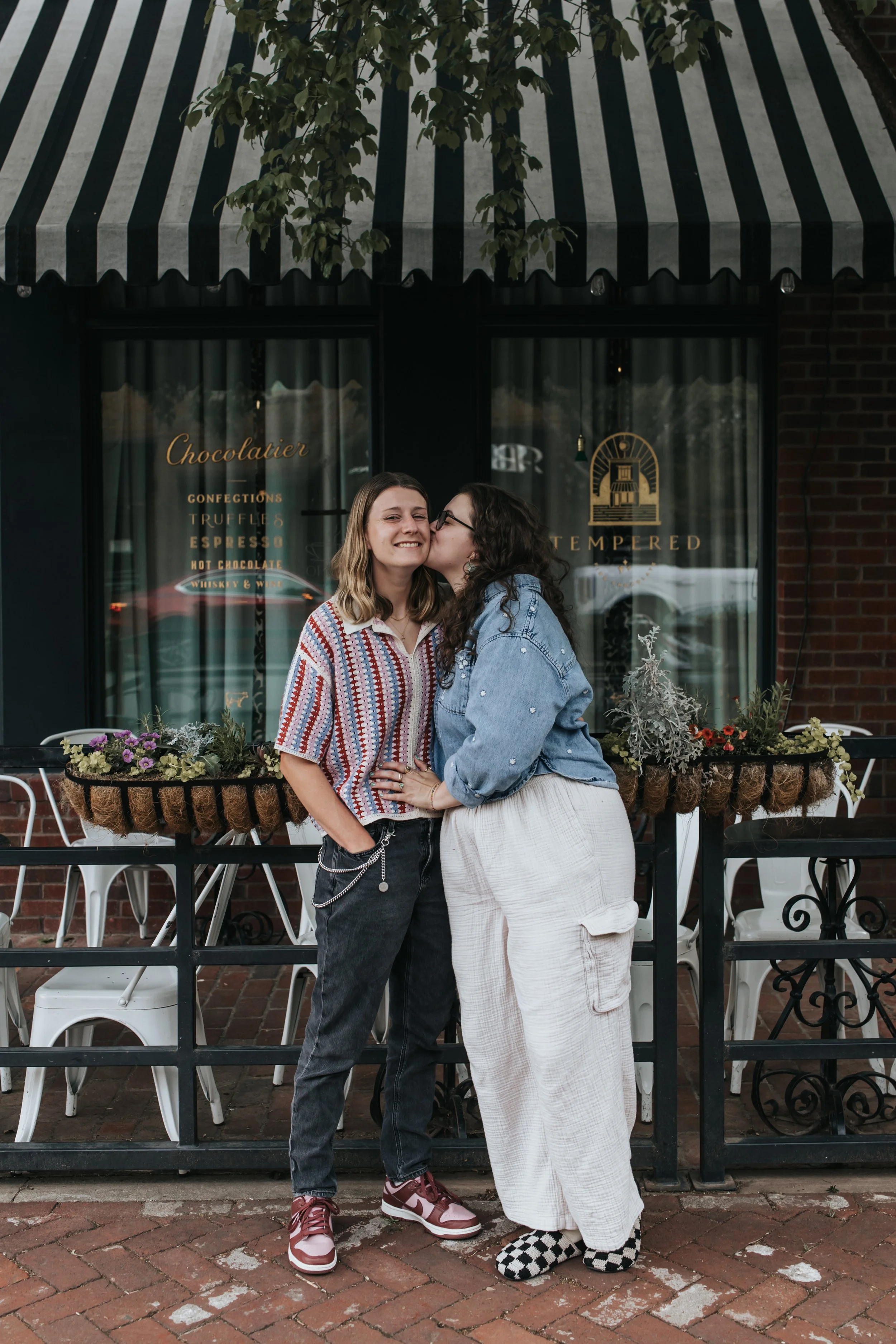  Maddie and Sarah, an LGBTQ+ couple in Nashville, kissing under an awning during their engagement photoshoot. 