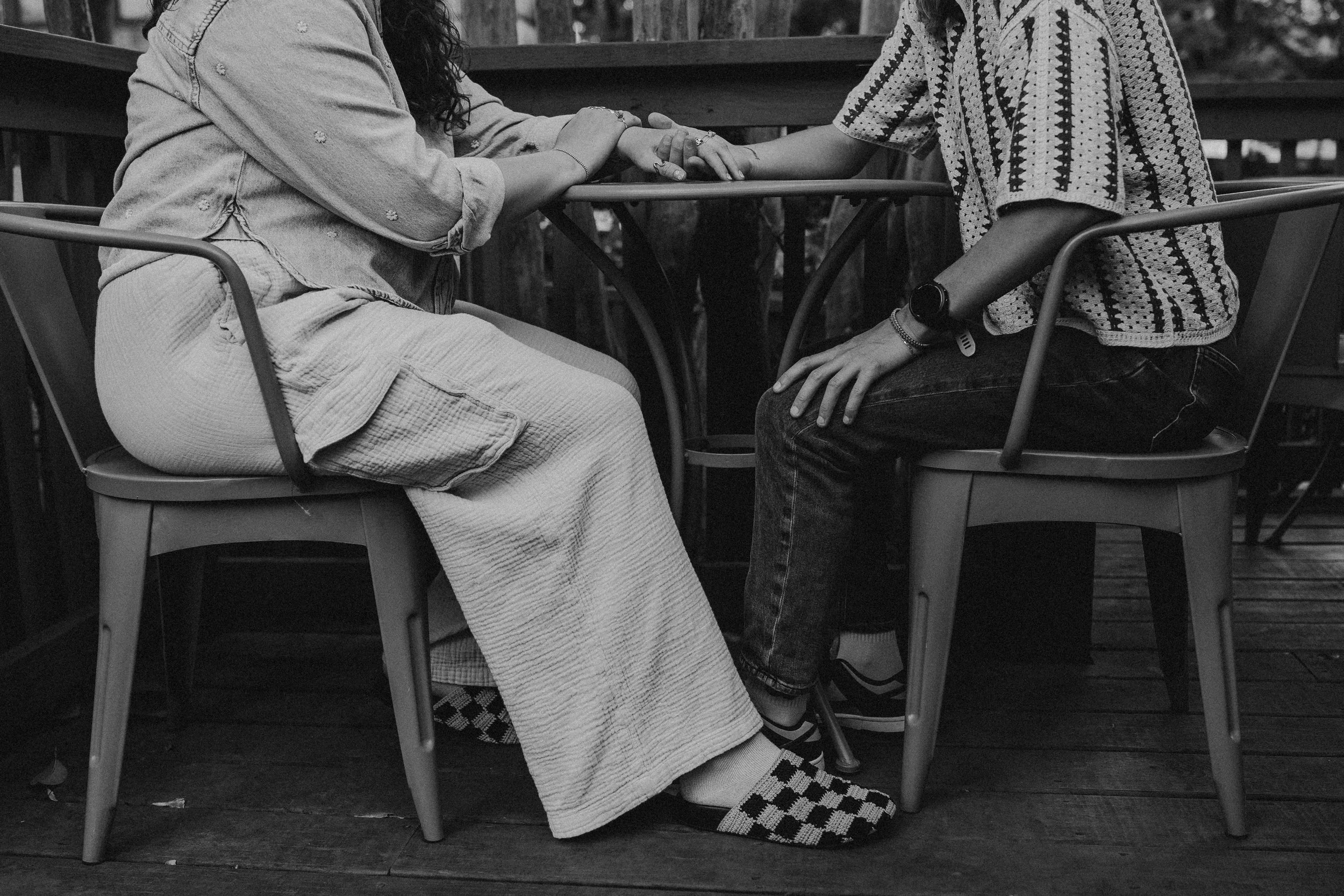  Black and white image of Maddie and Sarah’s legs while sitting at a coffee shop during their LGBTQ+ engagement photoshoot in Nashville. 