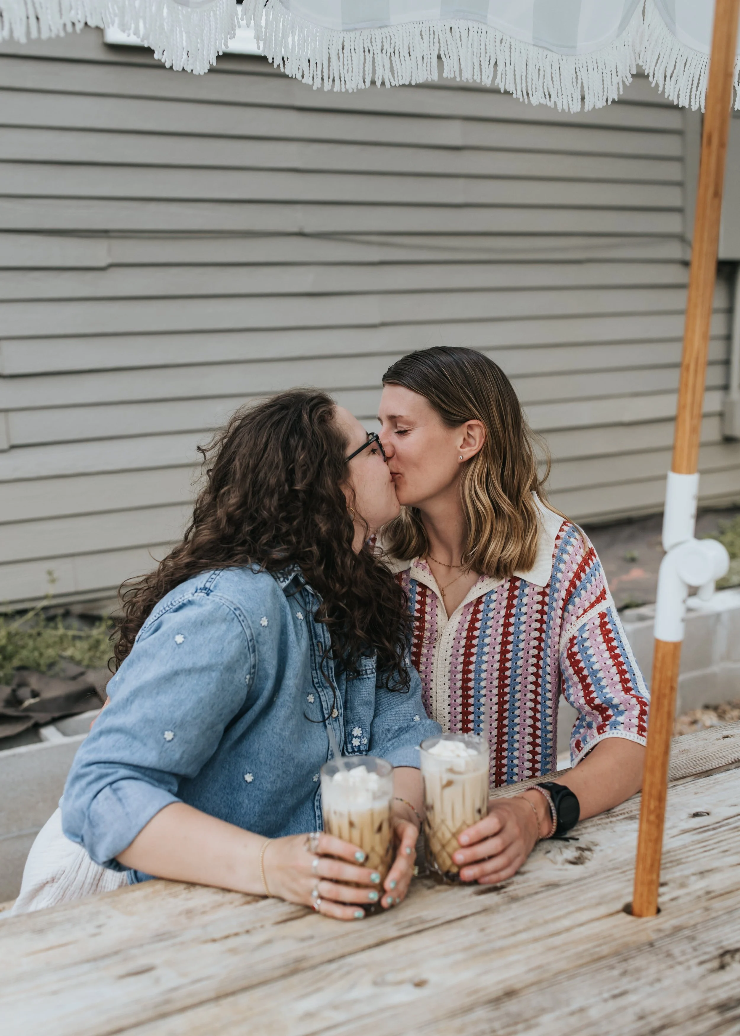  Maddie and Sarah kiss at a coffee shop during their engagement photoshoot, 