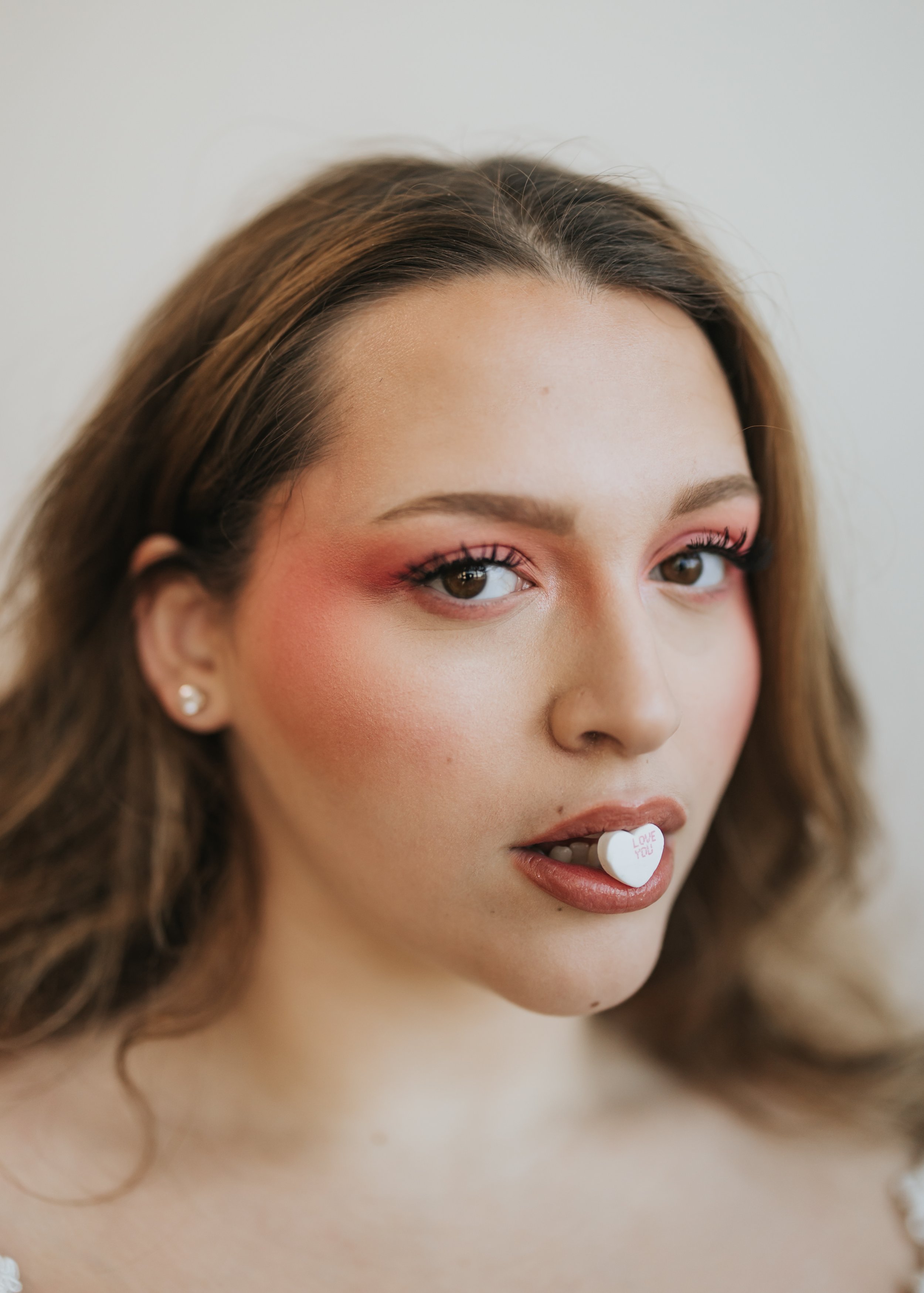 Close up photo of model with candy heart in her mouth for a creative Valentine’s Day fashion photoshoot.