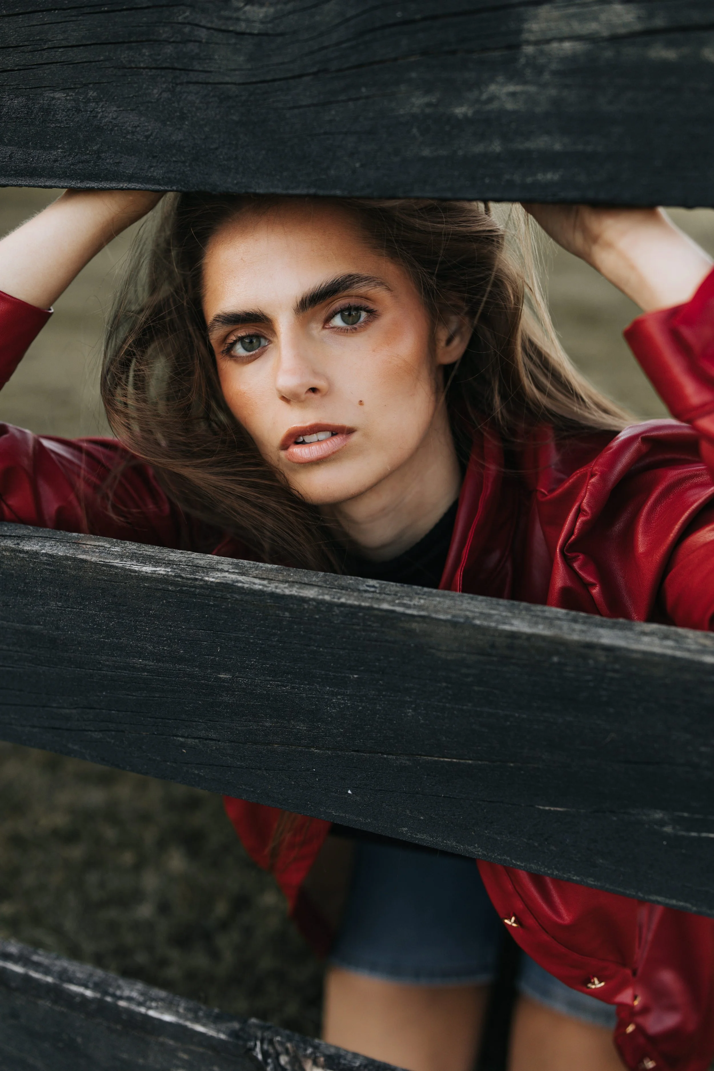  Model Skylar poses between a fence while wearing a red jacket during her Nashville fashion photoshoot. 