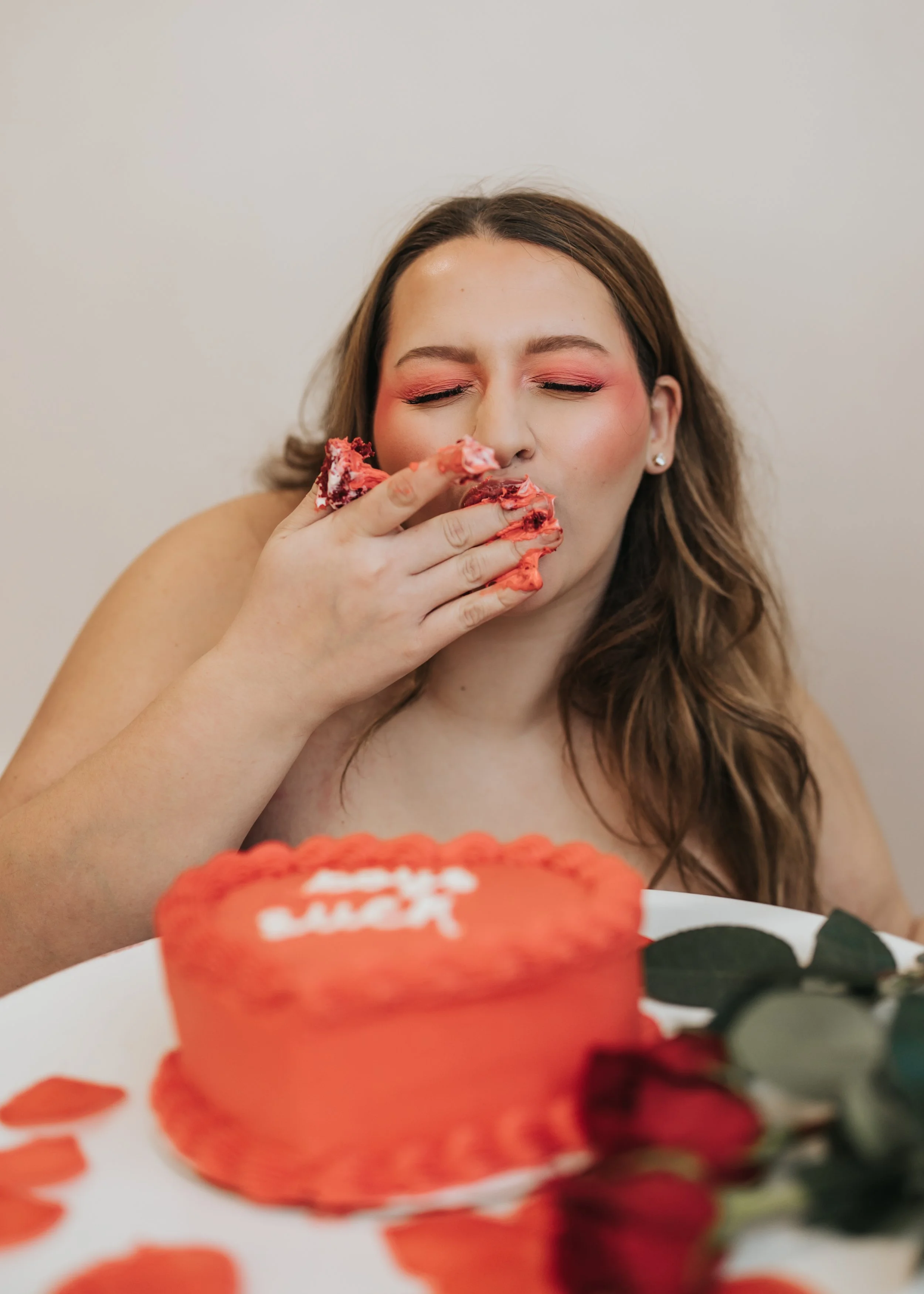 Fashion model poses with a heart-shaped cake while licking frosting from her hands for a creative Valentine’s Day photoshoot.