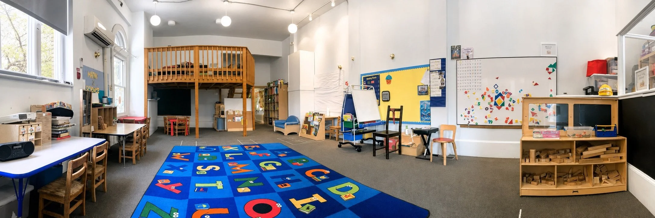 Bright early learning classroom with an alphabet rug, educational materials, activity tables, and building blocks