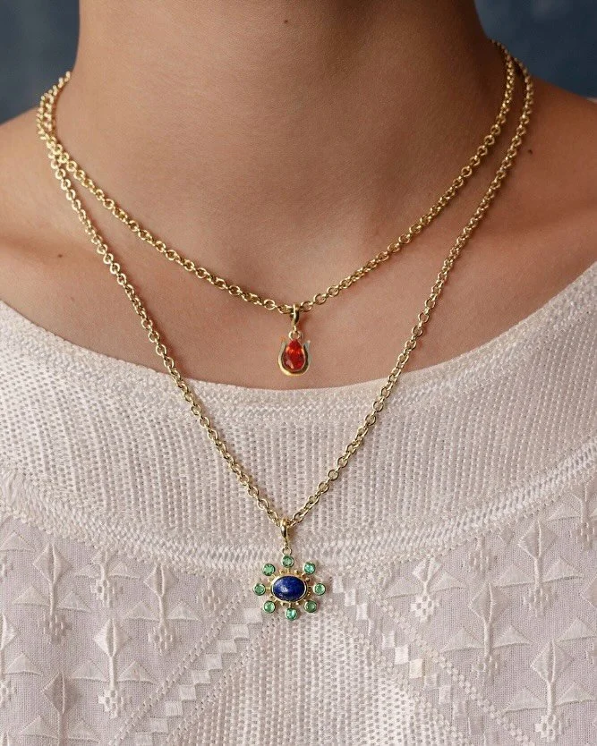 Our Tulip in orange sapphire, paired with our original Cosmos in lapis and emerald. I love them layered on our thick rolo chains &mdash; simple yet substantial. Always 18k Fairmined gold and responsibly sourced gemstones. Find your perfect pairing on