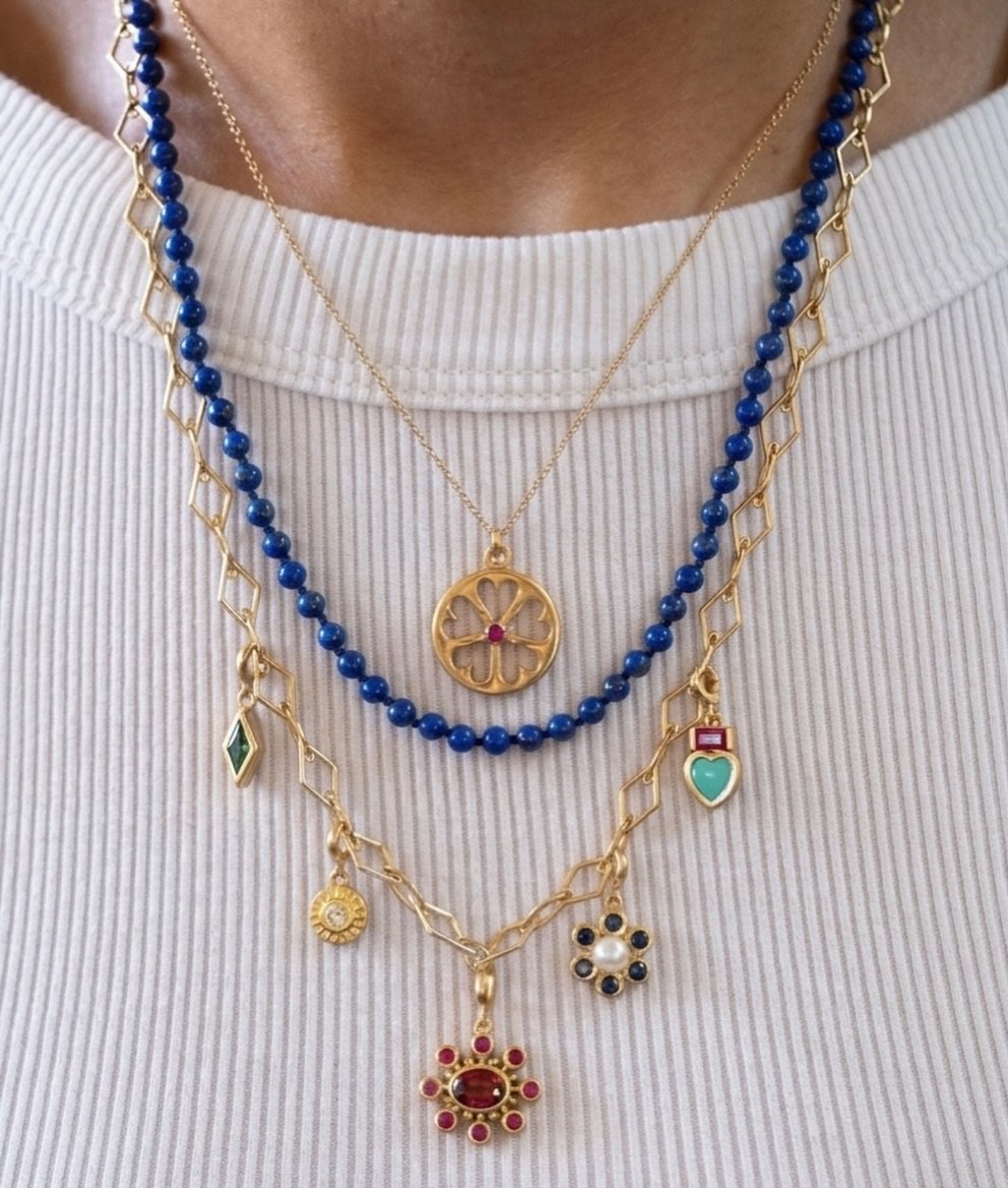 Our Tillya Tepe Heart Wheel, Lapis Bead Strand, and Zan Foundational Chain with our Zan charm in emerald, Sunburst charm in diamond, Cosmos charm in rhodolite and ruby, Pearly Flower charm in blue sapphire, and Tillya Tepe Heart charm in turquoise an