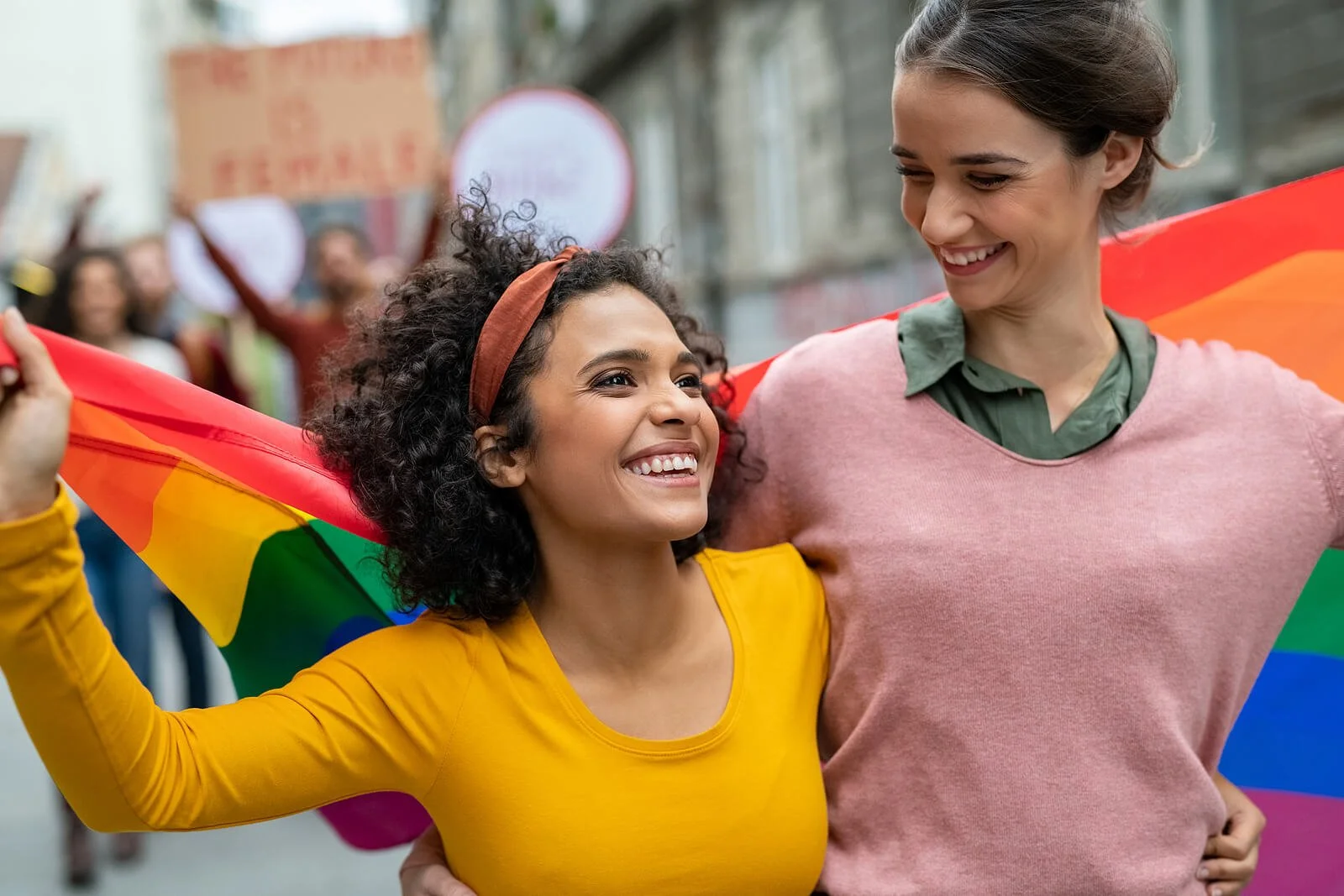 Two women smile joyfully with a pride flag, representing the connection made possible through LGBTQ therapy in San Diego, CA and EMDR therapy San Diego.
