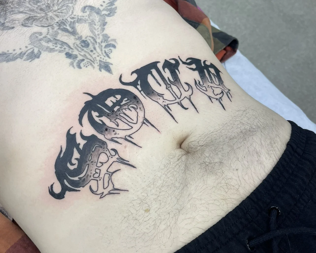Text tattoo over the stomach with black and grey shading.