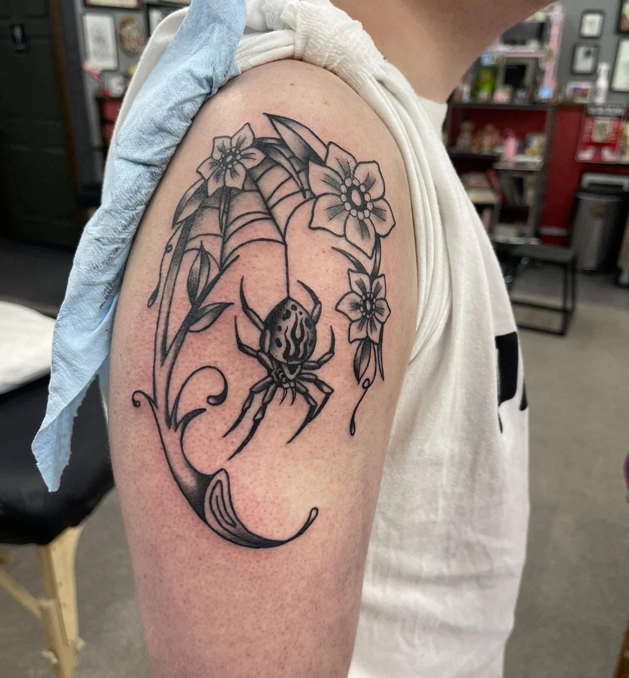 Black linework spider tattoo with a flower on the arm.