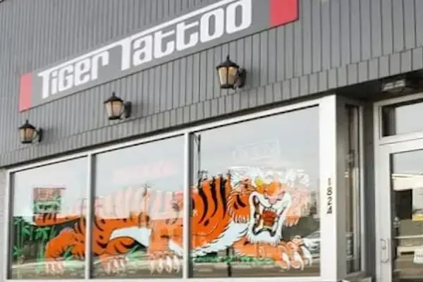 Front exterior of Tiger Tattoo shop in Spokane, WA showing storefront signage reading “Tiger Tattoo,” large front windows with a tiger graphic decal, and part of the entrance door visible.