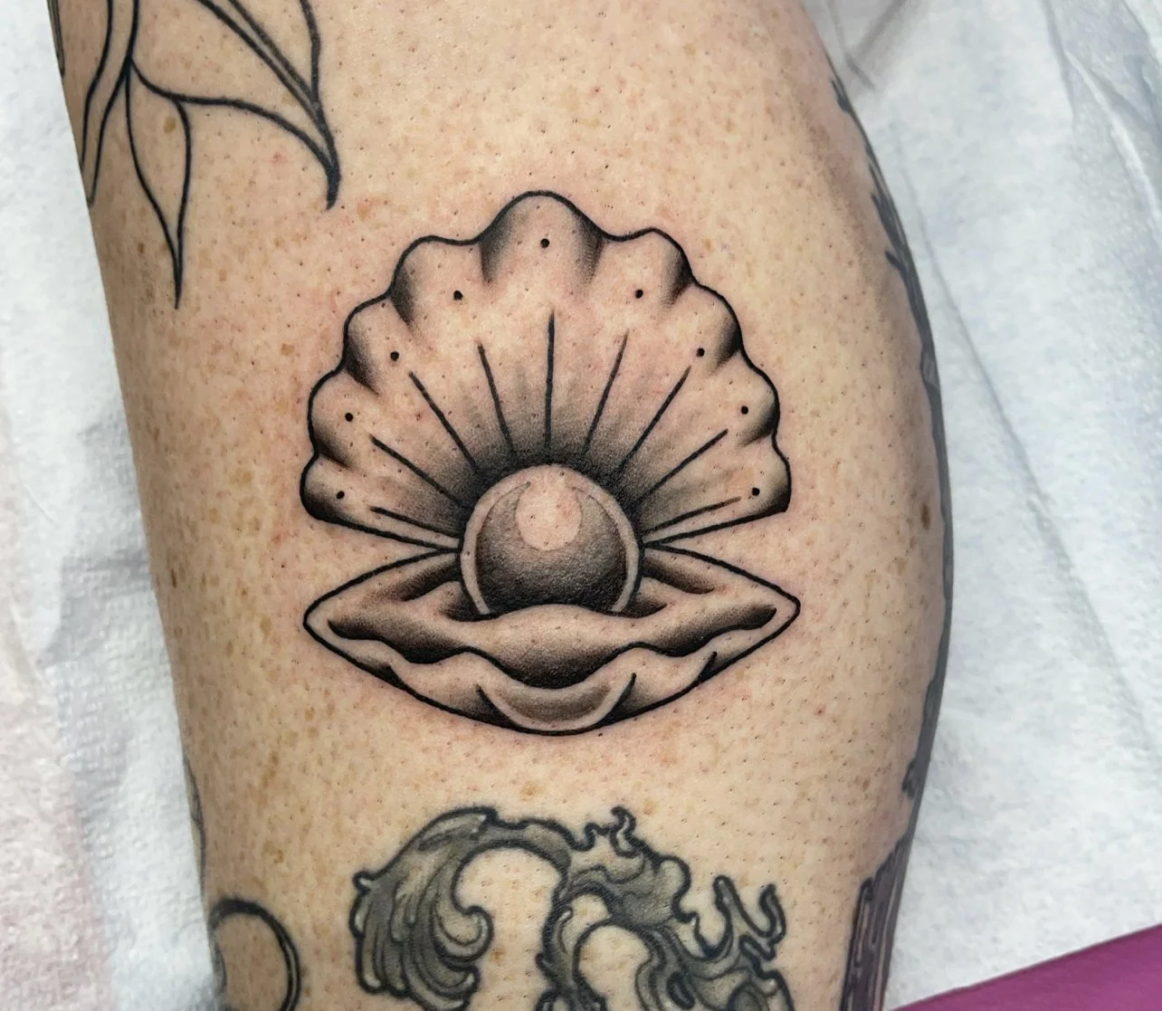 Pearl tattoo in a clam shell with black linework and shading on the leg.