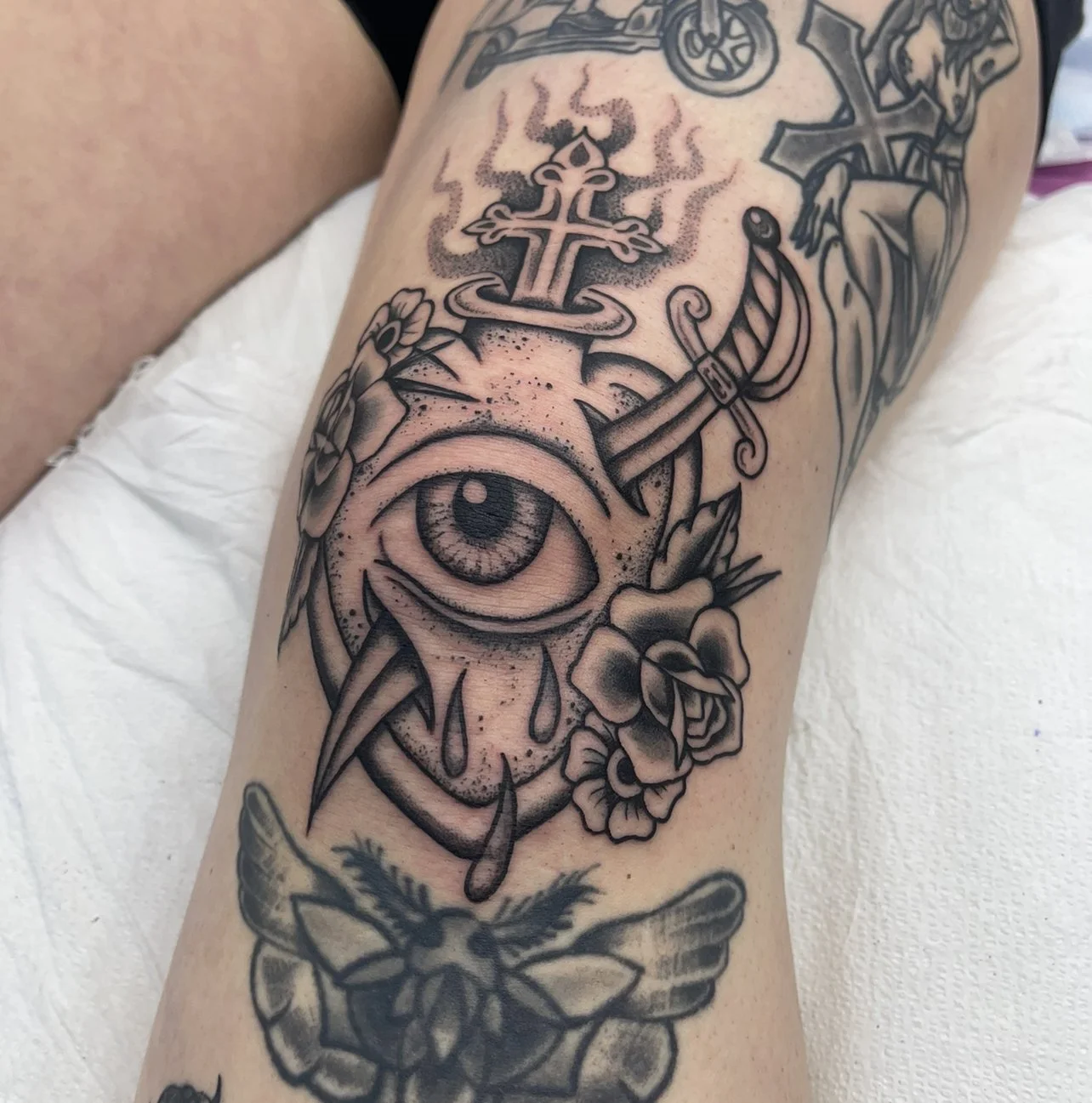 Eye on a heart with a cross and sword tattoo.
