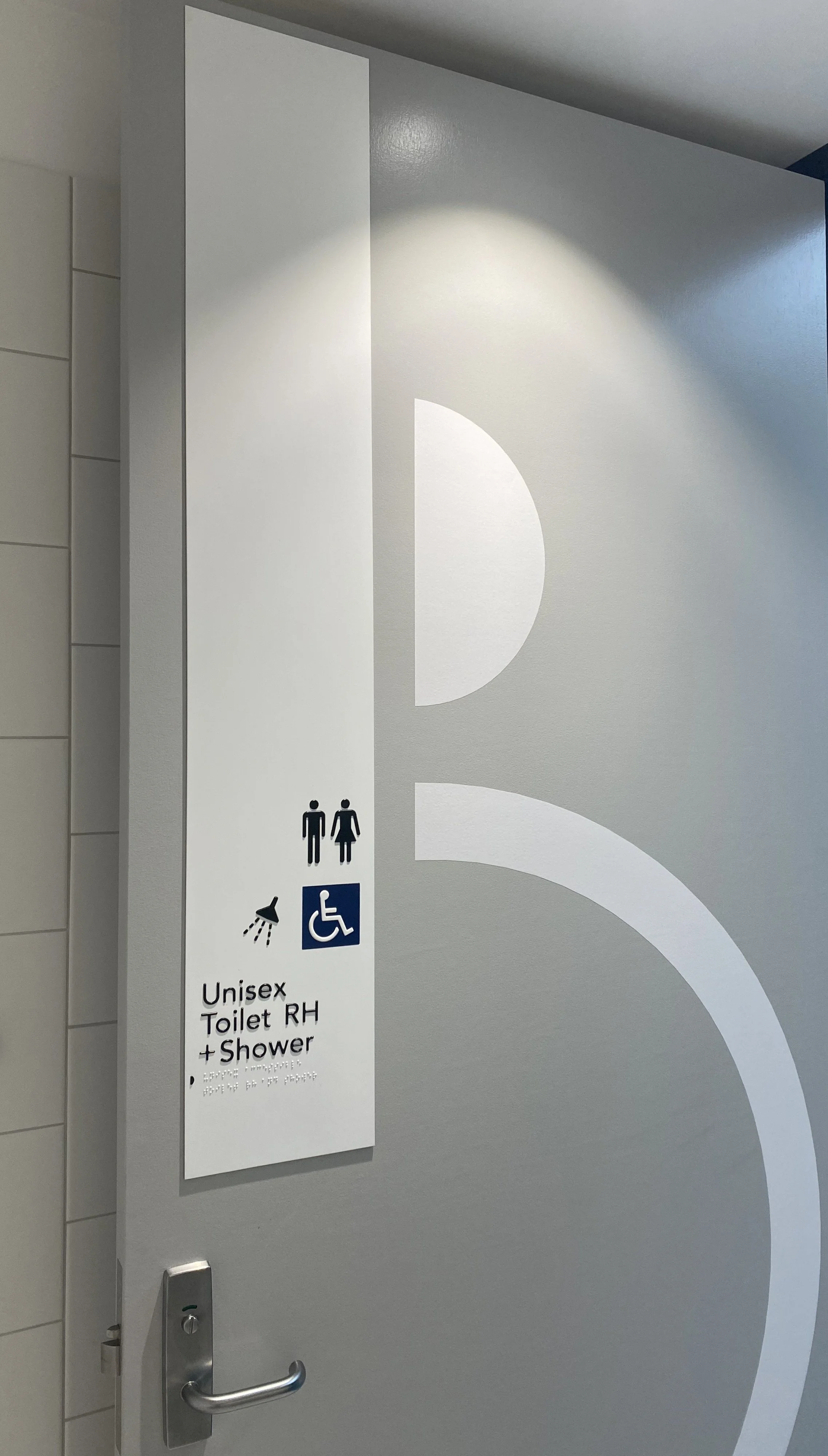 Sign on restroom door indicating unisex toilet with shower, accessible for wheelchair users, and includes male, female, and wheelchair symbols.