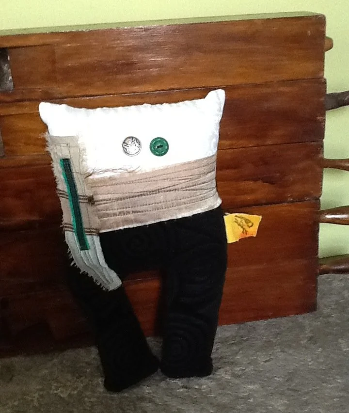 A pillow with a face, buttons for eyes, and pants, placed on a chair or bench.