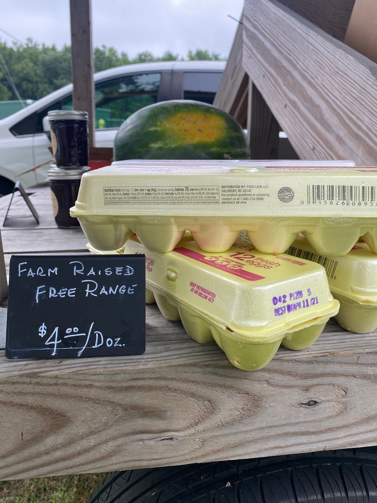 Six eggs in yellow cartons on a wooden table with a sign indicating they are farm raised and free range, priced at $4 per dozen.