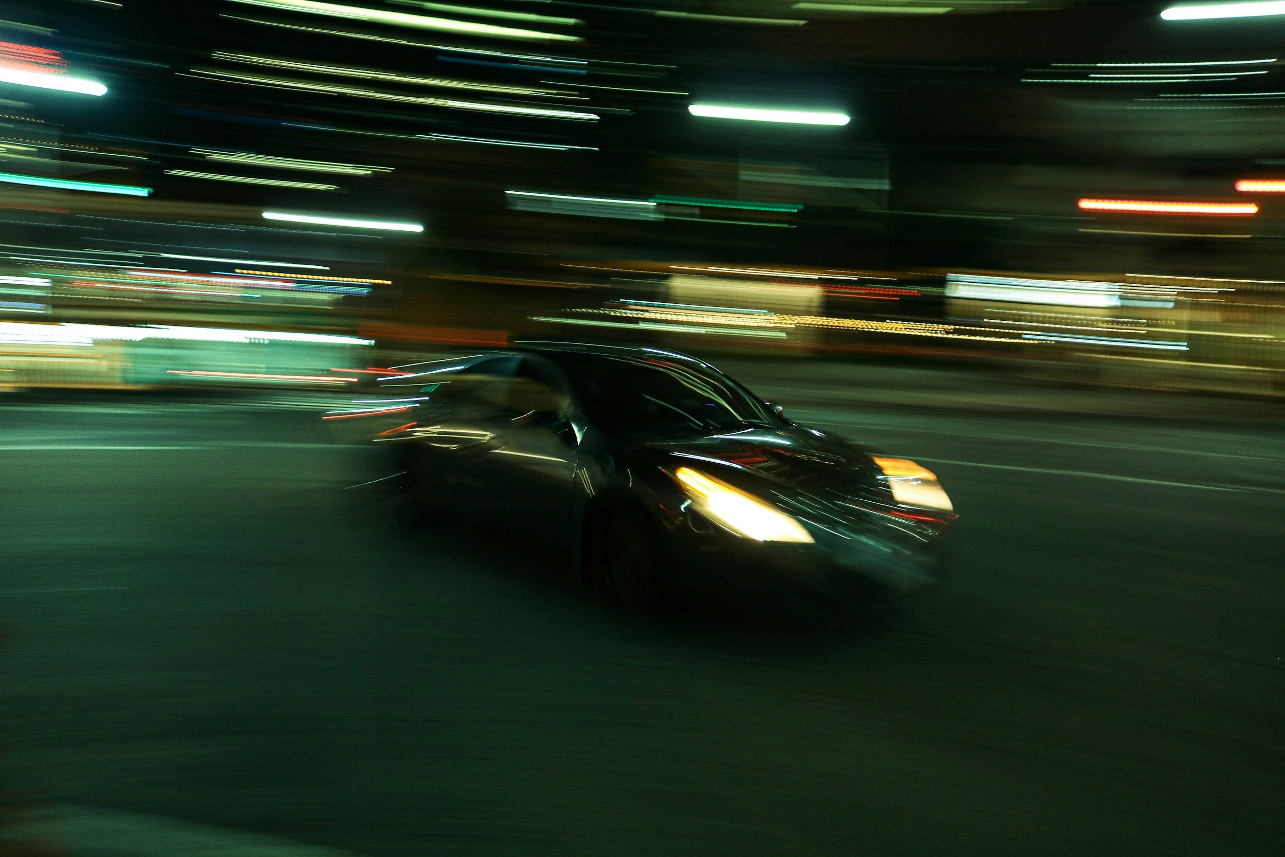 A black sports car driving at night with blurred city lights in the background
