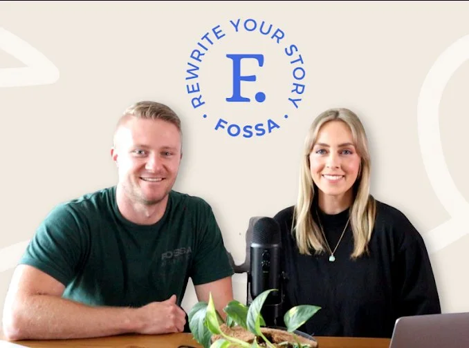 Two people sitting at a table with a microphone and a plant, with a Fossa logo and the text 'Rewrite Your Story' on the wall behind them.
