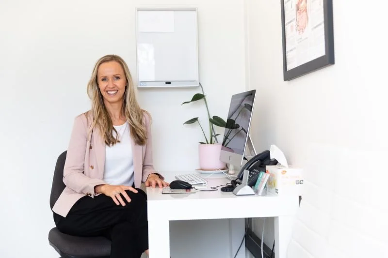 Person with glasses and dark hair wearing a black sweater, looking to the side in a bright room.