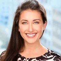 Smiling person with glasses and curly hair indoors.